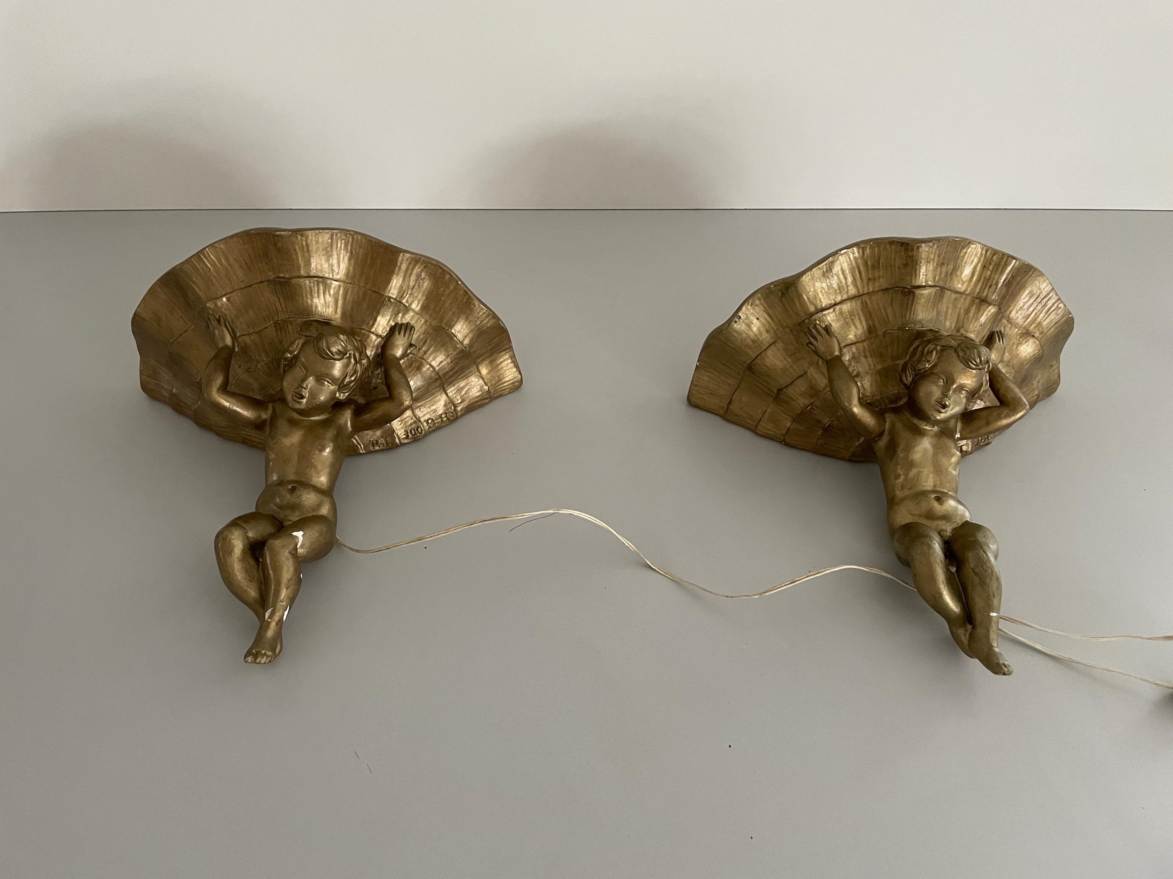 Made of Plaster Gold Coloured Pair of Sconces in Angel Sculpture, 1960s, Italy

Lampshade is in very good vintage condition.

Note: Some small parts on the lamp were damaged due to wear and were immediately glued on. some small pieces are still