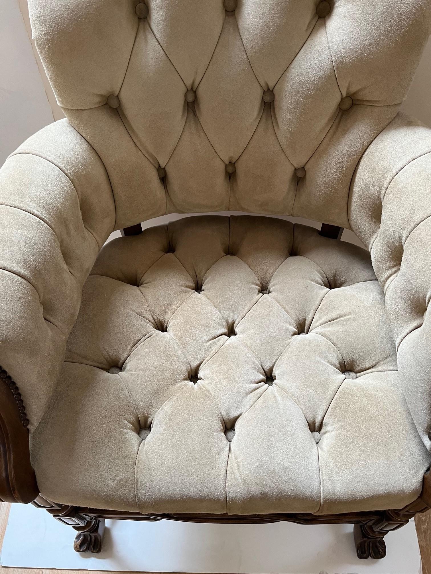 Made to Order Elegant Seville Armchair Upholstered in Beige Suede Leather, Tufted Seat and Back, Petite Antique Brass Nail Head Trim at Seat, Arms, and outside back, Carved Hardwood Frame with Front Stretcher Finished in Medium Walnut. This is a