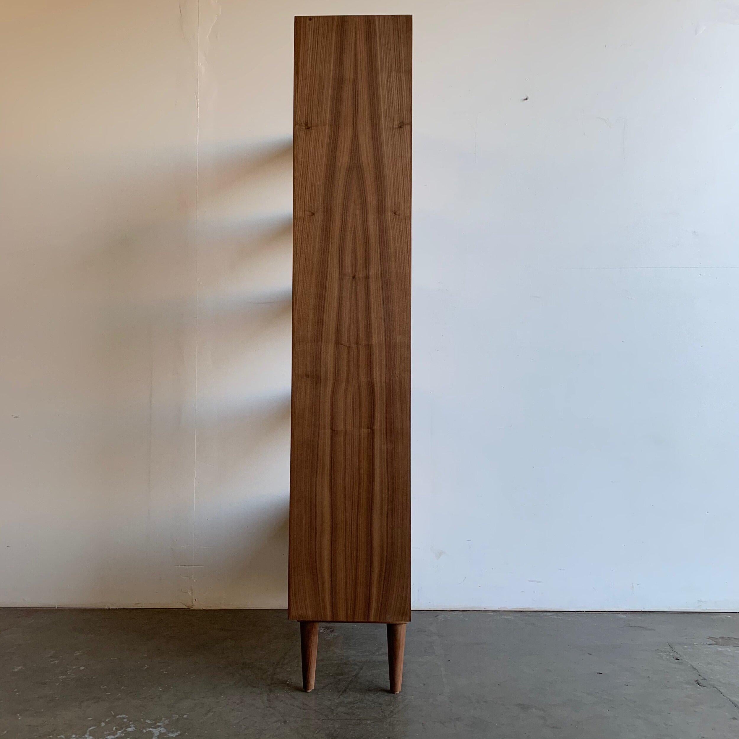 12.25D

32.25W

68.75H

Made of walnut veneer over a solid plywood. They are custom made and only available upon request. There is a 3week to 7week lead time. This can also be made out of solid wood, and other woods such as white oak, birch or oak.