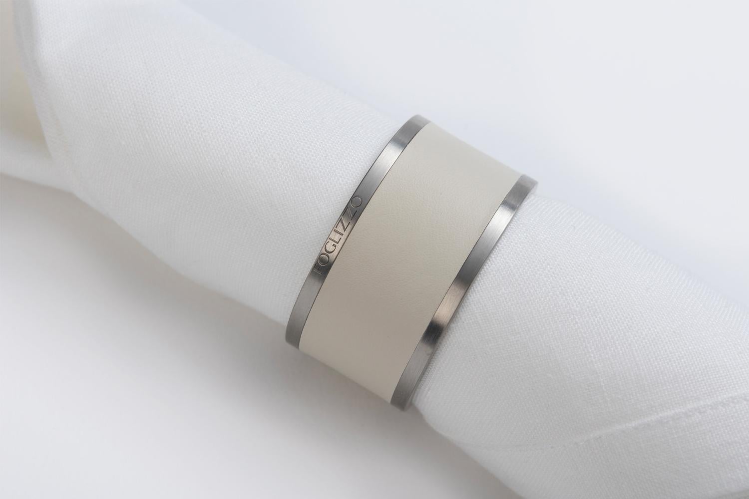 Il portatovagliolo dal design minimo dona un accento sorprendente su tavoli moderni o classici. La semplice silhouette è realizzata in acciaio inossidabile, parzialmente rivestita con esclusiva pelle Foglizzo.
