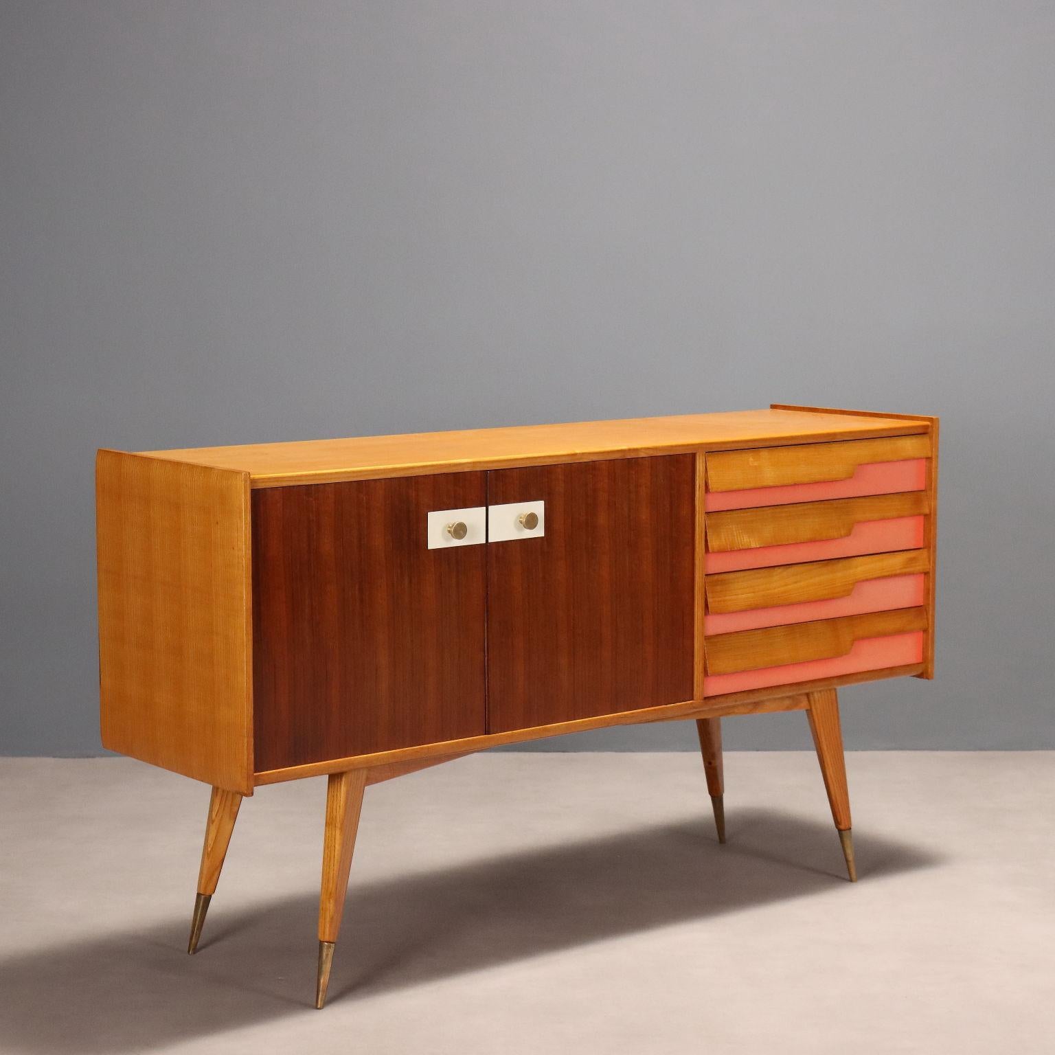 Arredo vintage di manifattura italiana del XX secolo restaurato nei nostri laboratori, in legno di frassino con impiallacciatura in mogano e inserti in formica. Presenta due ante a battente e quattro cassetti; maniglie e puntali delle gambe in