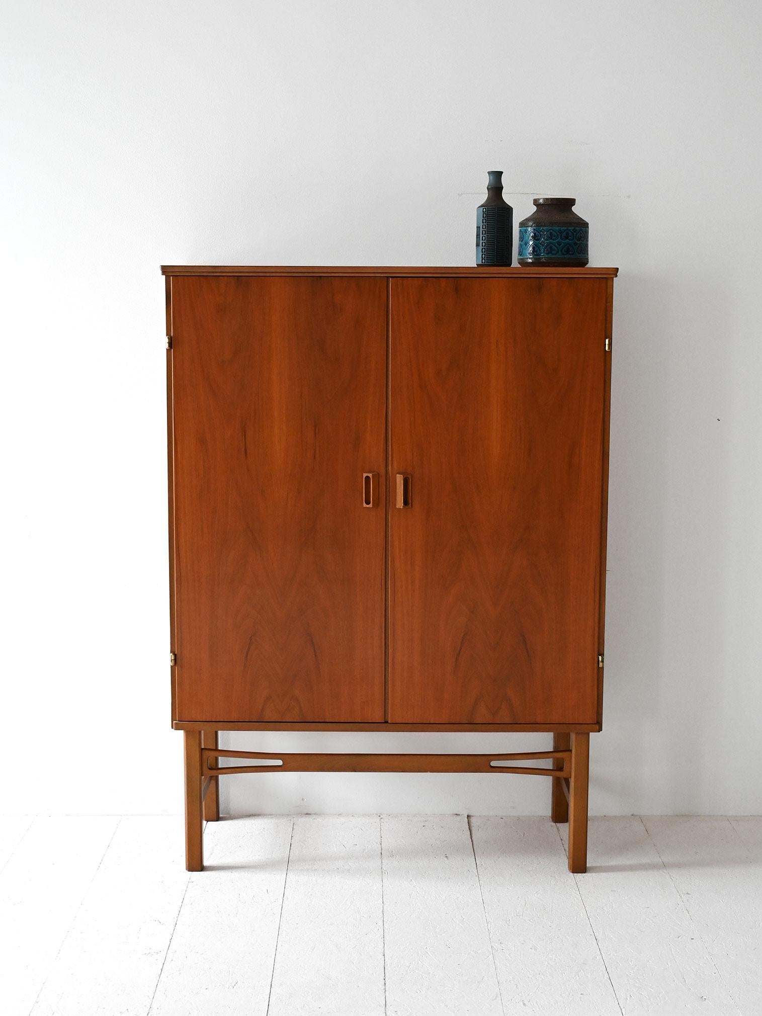 Vintage teak cabinet with two hinged doors and wooden handles. Linear legs lighten the figure. 

Inside the cabinet, the space is divided by two shelves while small pull-out shelves are located at the bottom. Good conditions. Potrebbe presentare dei