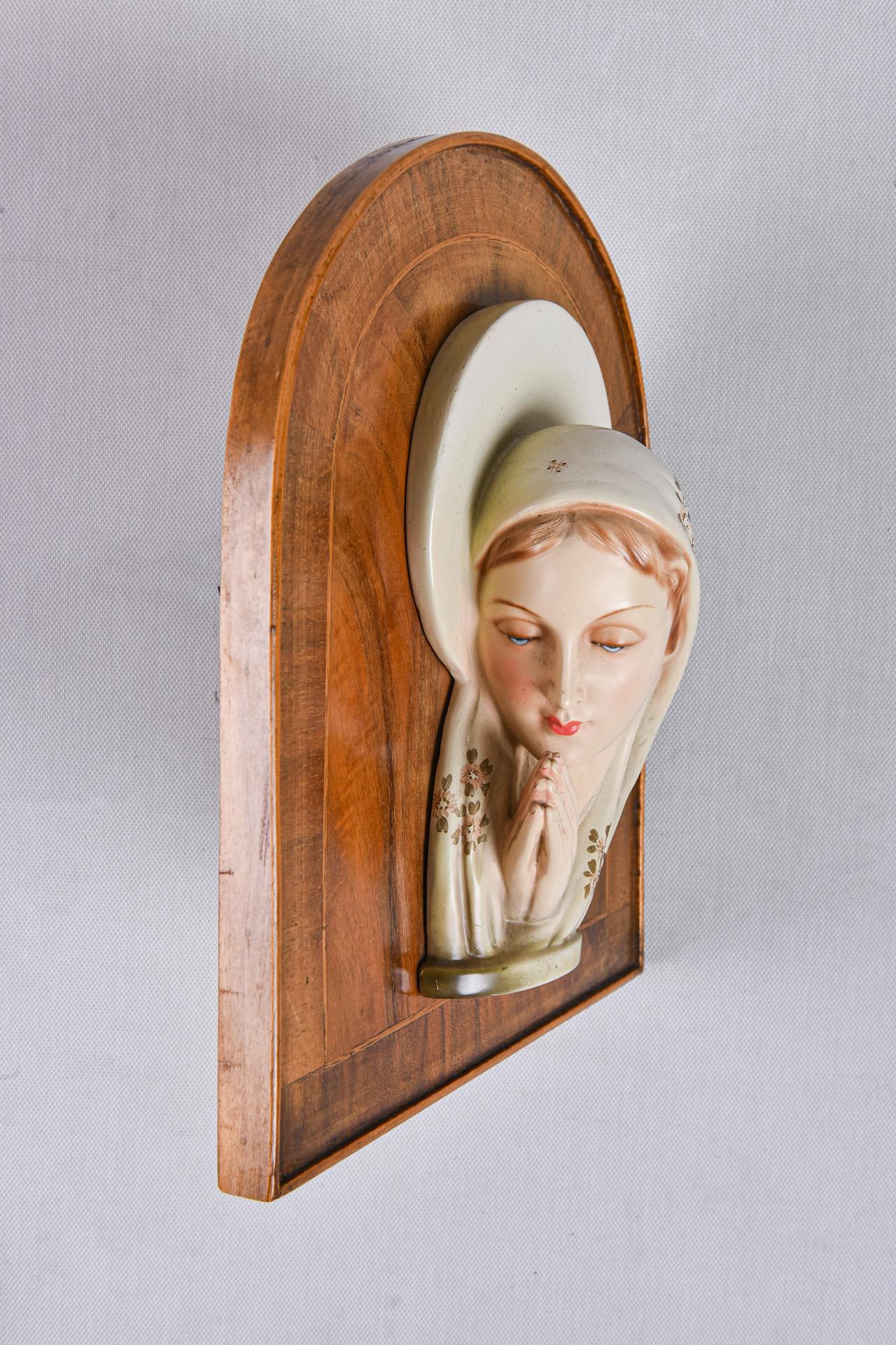 Madonna in keramischem Hoch- oder Flachrelief auf einem Holzpaneelsockel, aus der Déco-Zeit.  Auf den Schleier der Madonna sind kleine Blumen gemalt.
Es ist köstlich!