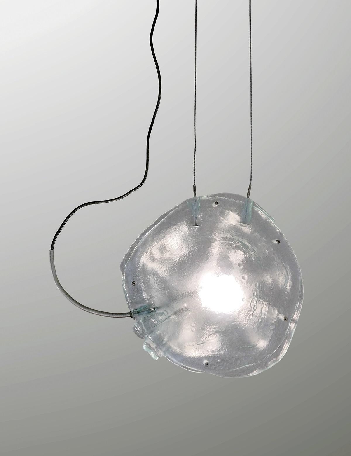 Lampada a sospensione Madreperla II di A. Moreno
Fatto a mano
Dimensioni: D 25 x L 40 x H 40 cm.
Materiali: Vetro.

Lampada da soffitto realizzata con i resti di vecchie finestre, modellate con un processo simile alla cremazione umana e sottoposte a