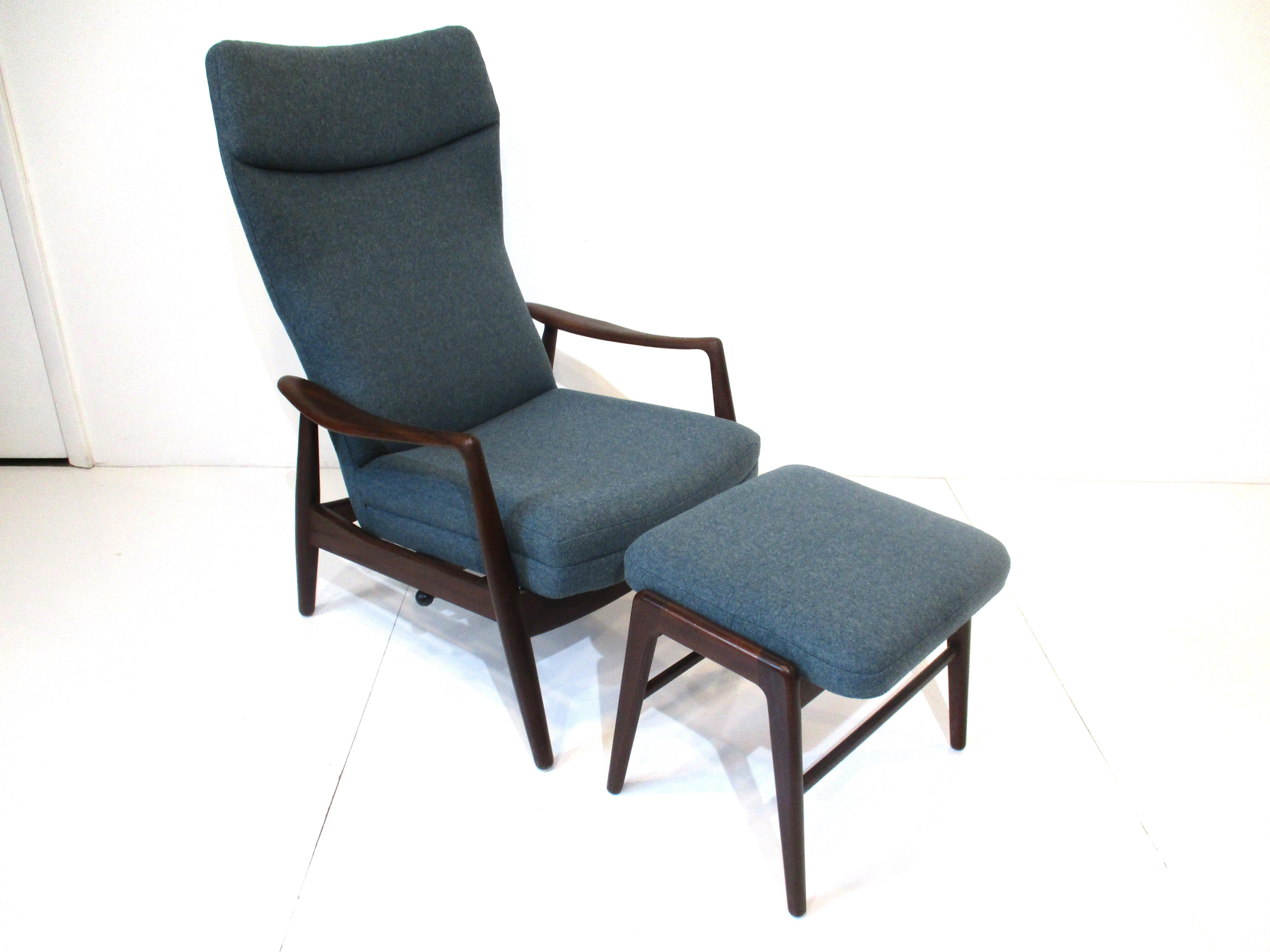 A finely crafted dark teak wood framed lounge chair with sculptural armrests and winged styled backrest with matching ottoman reupholstered in a wool blend Danish steel gray blue fabric. One of the most comfortable lounge chairs we have had with