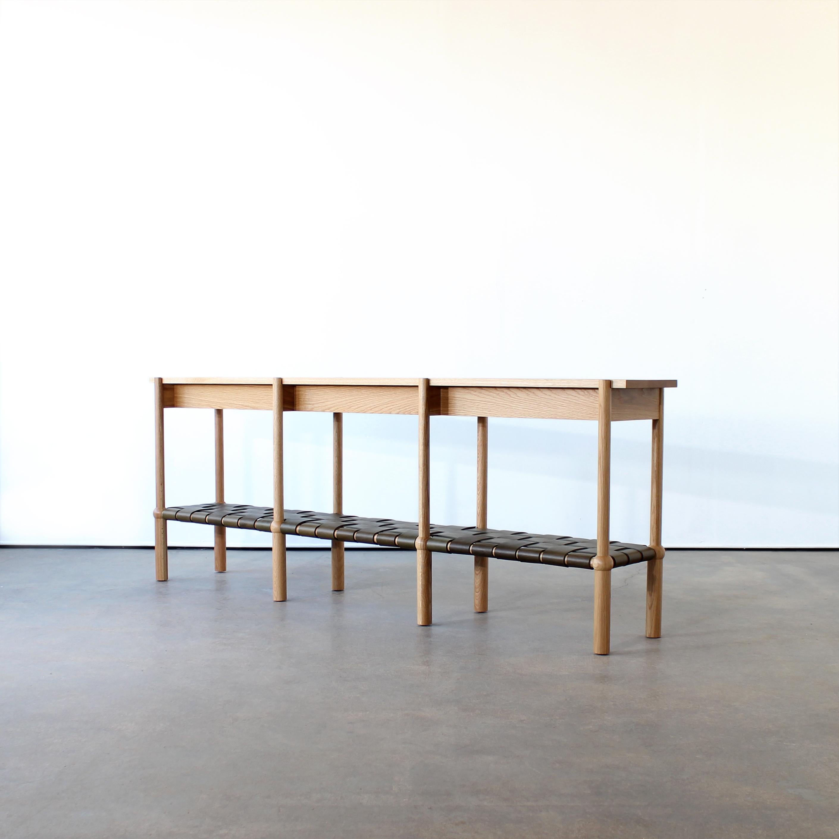 Mae console table by Crump and Kwash 

Hand turned, solid wood legs and cross members / Solid wood top / Veg tan woven leather shelf / Customizations available.

Options 
Wood - White Oak, Walnut, Maple, Black Oak 
Leather - Olive, Black, Hickory