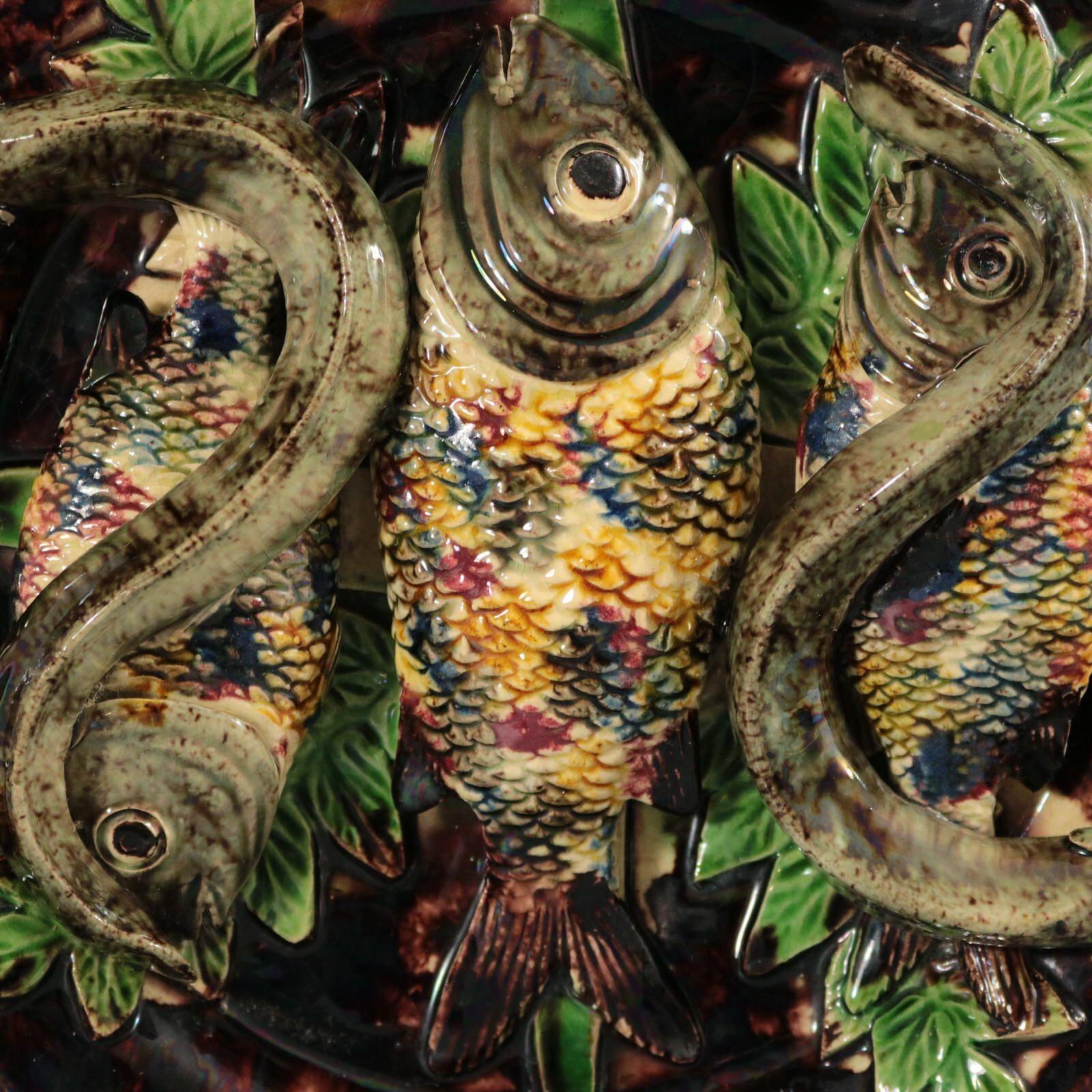 Wandteller aus Majolika von Mafra mit drei Fischen und zwei Aalen, die auf Blättern liegen. Muscheln rund um die Grenze. Färbung: Braun, grün, grau, sind vorherrschend. Das Stück trägt Herstellermarken für die Töpferei von Mafra.