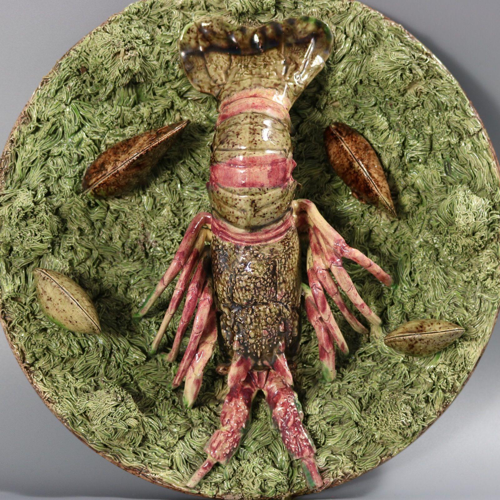 Mafra Portuguese Palissy Majolica wall plate which features a lobster and four shells, sitting on an extruded clay ground. Colouration: green, brown, pink, are predominant. The piece bears maker's marks for the Mafra pottery.