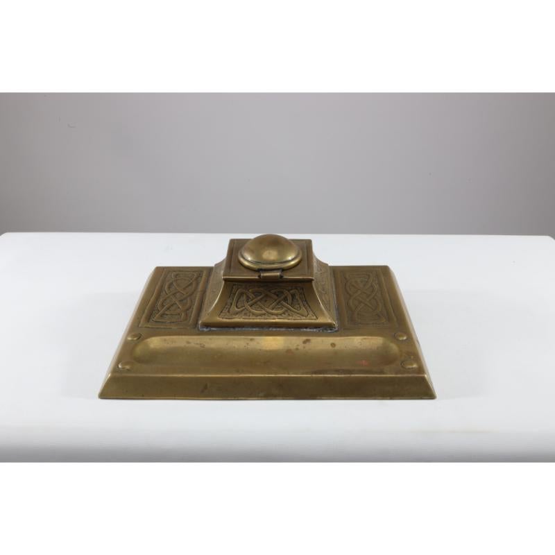 Magaret Gilmour School. An Arts & Crafts brass inkwell with a dome lid and Celtic interlacing around the inkwell body and to each side of the base with a shallow pen holder at the front. Lacking inkwell.