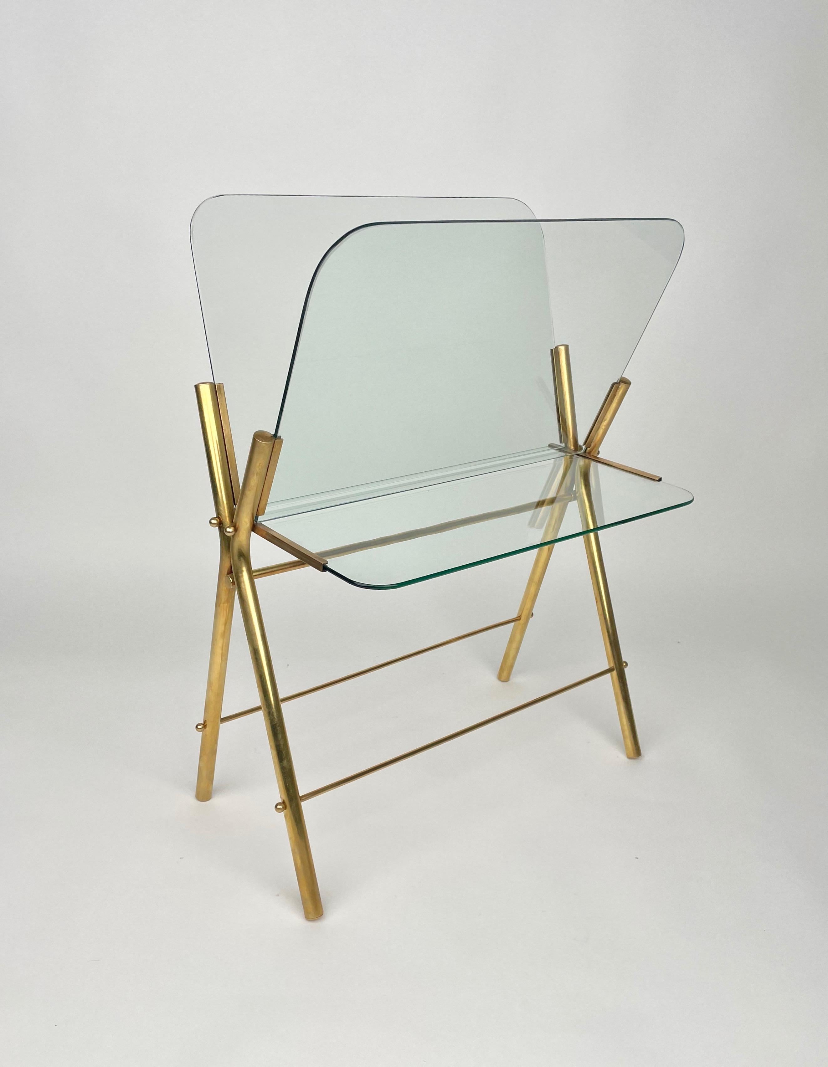 Magazine rack stand in a brass and glass structure which can also be used as a table as it features a glass shelf.

Made in Italy in the 1950s.