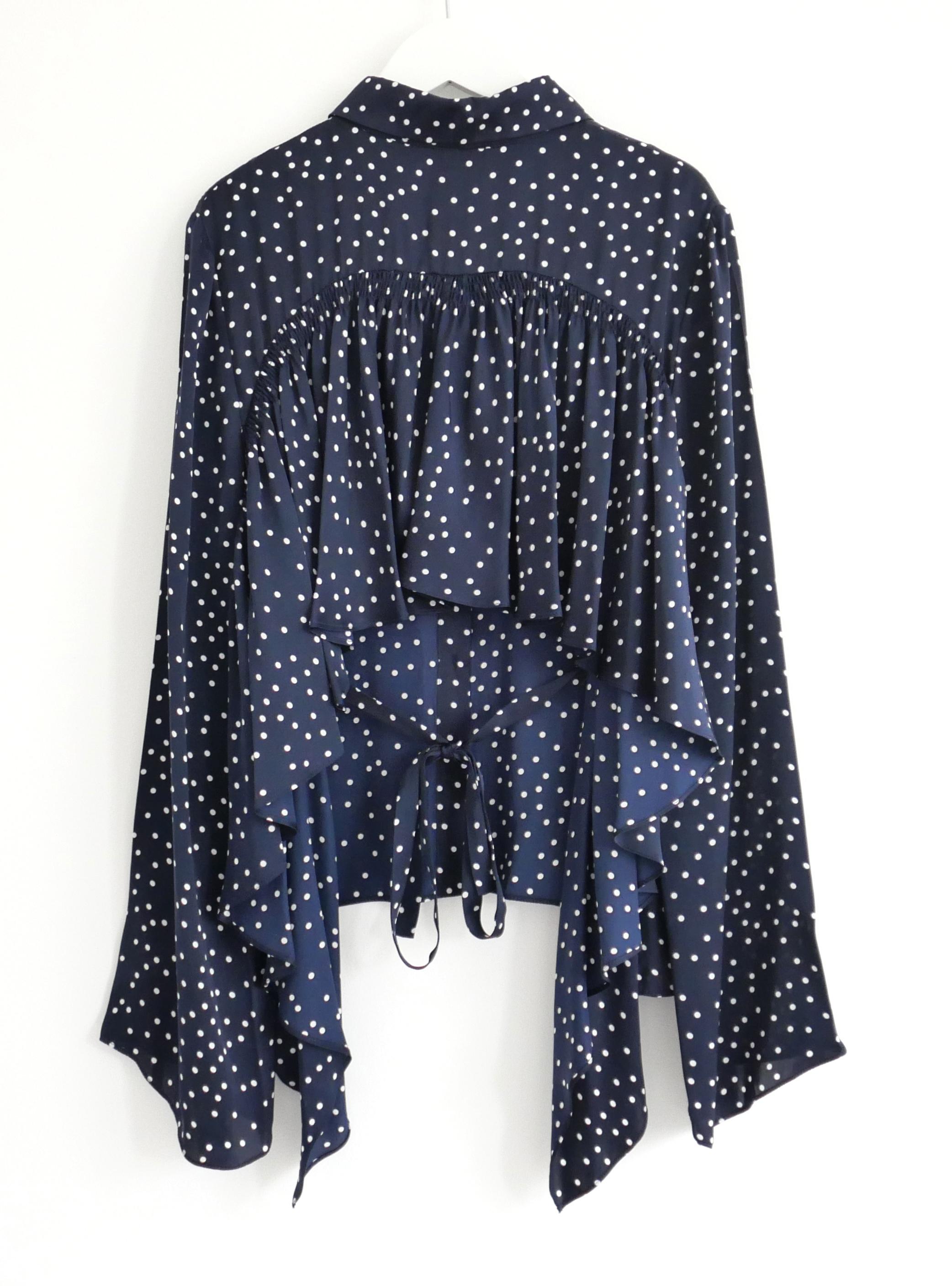 Impresionante blusa de seda de lunares Orleans de Magda Butrym. Confeccionado en seda supersuave con estampado de lunares nay y blanco, tiene un corte holgado con la espalda abierta con volantes, lazos en la cintura y mangas anchas. Talla FR36/UK8.