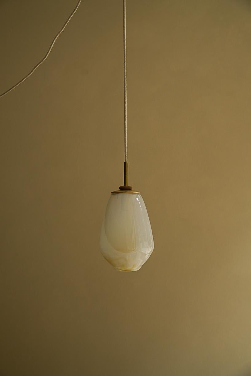 Magena II Pending Lamp by La Lune
Dimensions: Ø 16 x H 22 cm. 
Materials: Blown glass, linen cable, brass piece and turned wood ring.

Produced in France. Custom sizes available. Also available in different shapes. Please contact us.

La Lune is