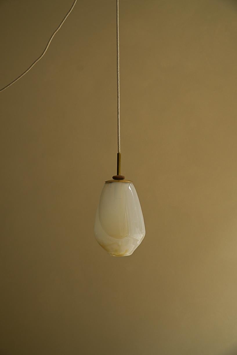 Lámpara Pendiente Magena II by La Lune
Dimensiones: Ø 16 x A 22 cm. 
Materiales: Vidrio soplado, cable de lino, pieza de latón y aro de madera torneada.

Producido en Francia. Tamaños personalizados disponibles. 
También disponible en diferentes