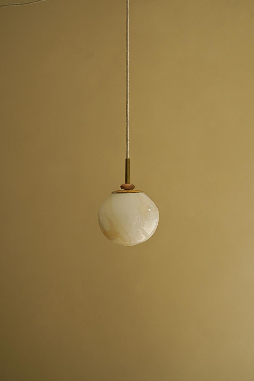 Magena IV Pending Lamp by La Lune
Dimensions: Ø 15 x H 13 cm. 
Materials: Blown glass, linen cable, brass piece and turned wood ring.

Produced in France. Custom sizes available. Also available in different shapes. Please contact us.

La Lune is