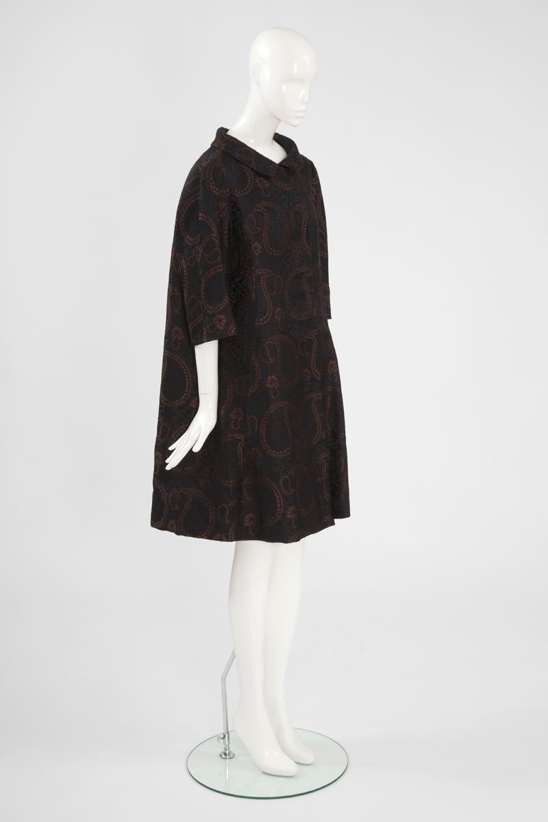 Perfect for a formal event, this elegant late 50’s - early 60’s Maggy Rouff coat is a classic outwear piece which will enhance any contemporary wardrobe. Constructed in black jacquard silk with a brown rust paisley motif, this coat features an