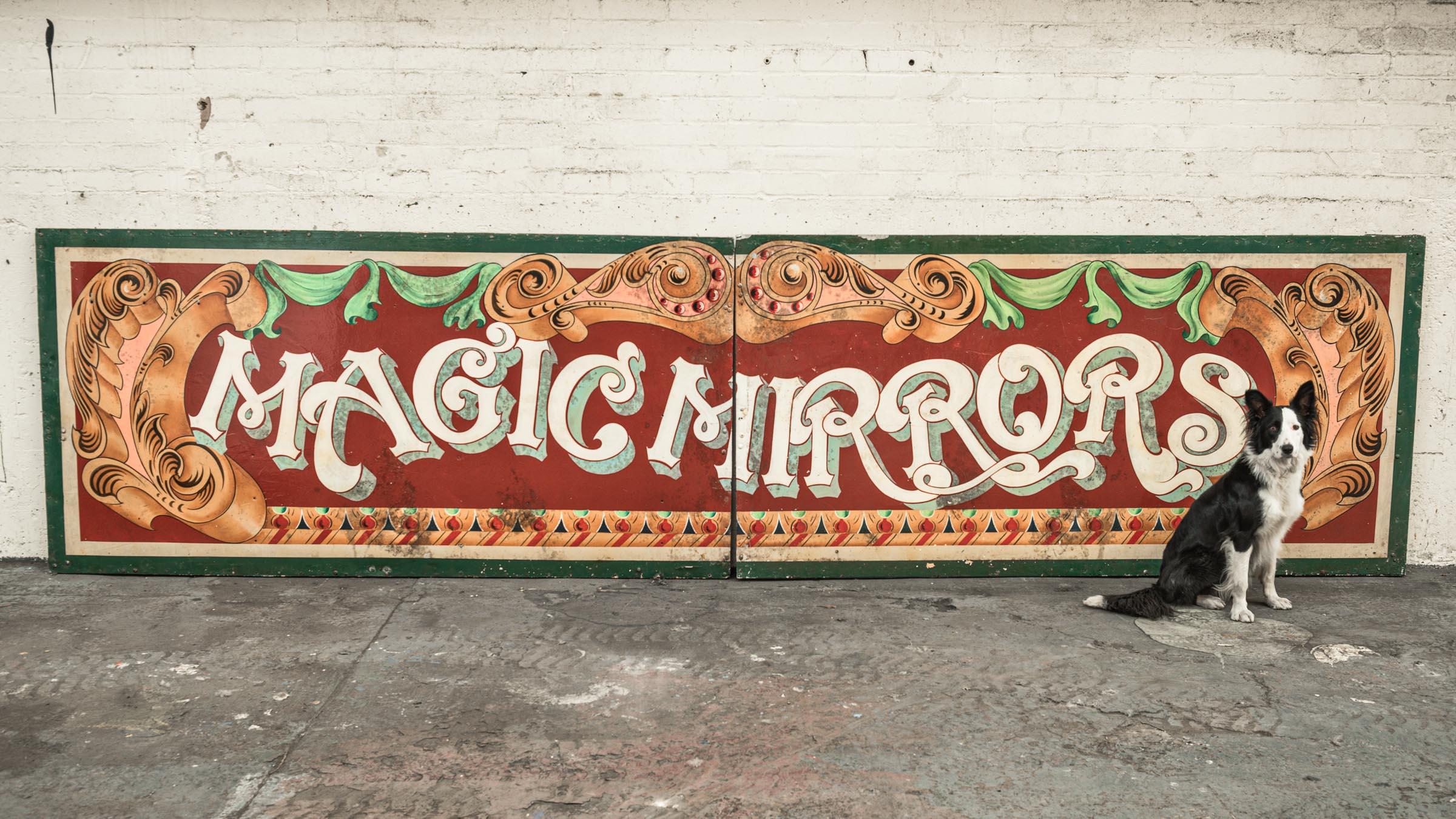 A glorious piece of English fairground history and a great tribute to the art form that developed around this genre. 

This hand painted large wooden framed metal plate 'Magic Mirrors' fun fair hoarding originated from the town of
