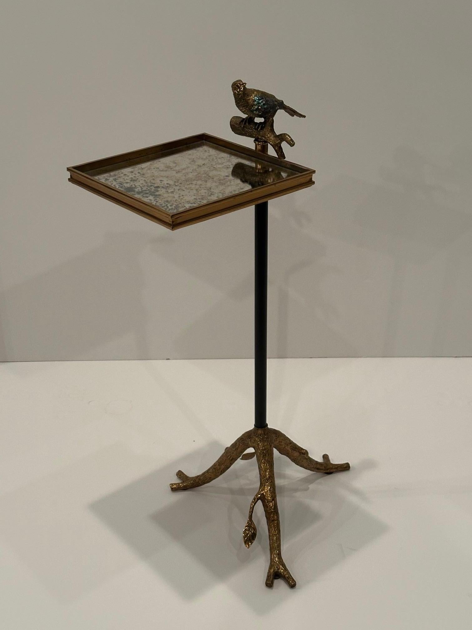 Il tavolo d'accento Maitland Smith Tweet ha un magico mix di gambe scultoree a forma di ramoscello in bronzo, un piccolo piano quadrato con specchio invecchiato e un uccello intarsiato che vi si posa.  È un meraviglioso tavolo da Martini e un'opera