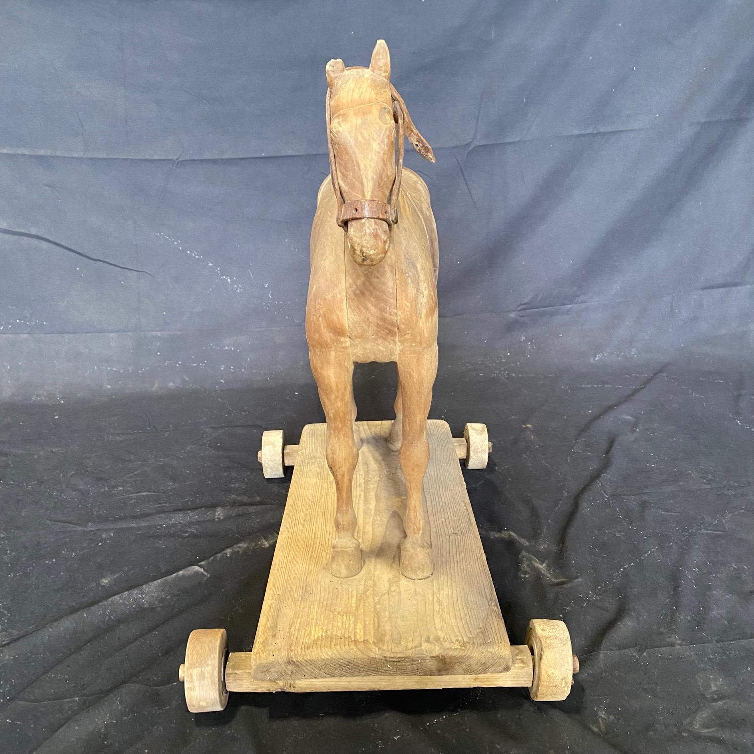 Late 19th century oversized pull along horse toy. A stunning handmade example with unusually large propositions. Stands on original wooden pull along base with functioning wooden wheels. A sculptural work of art bought in the South of France.