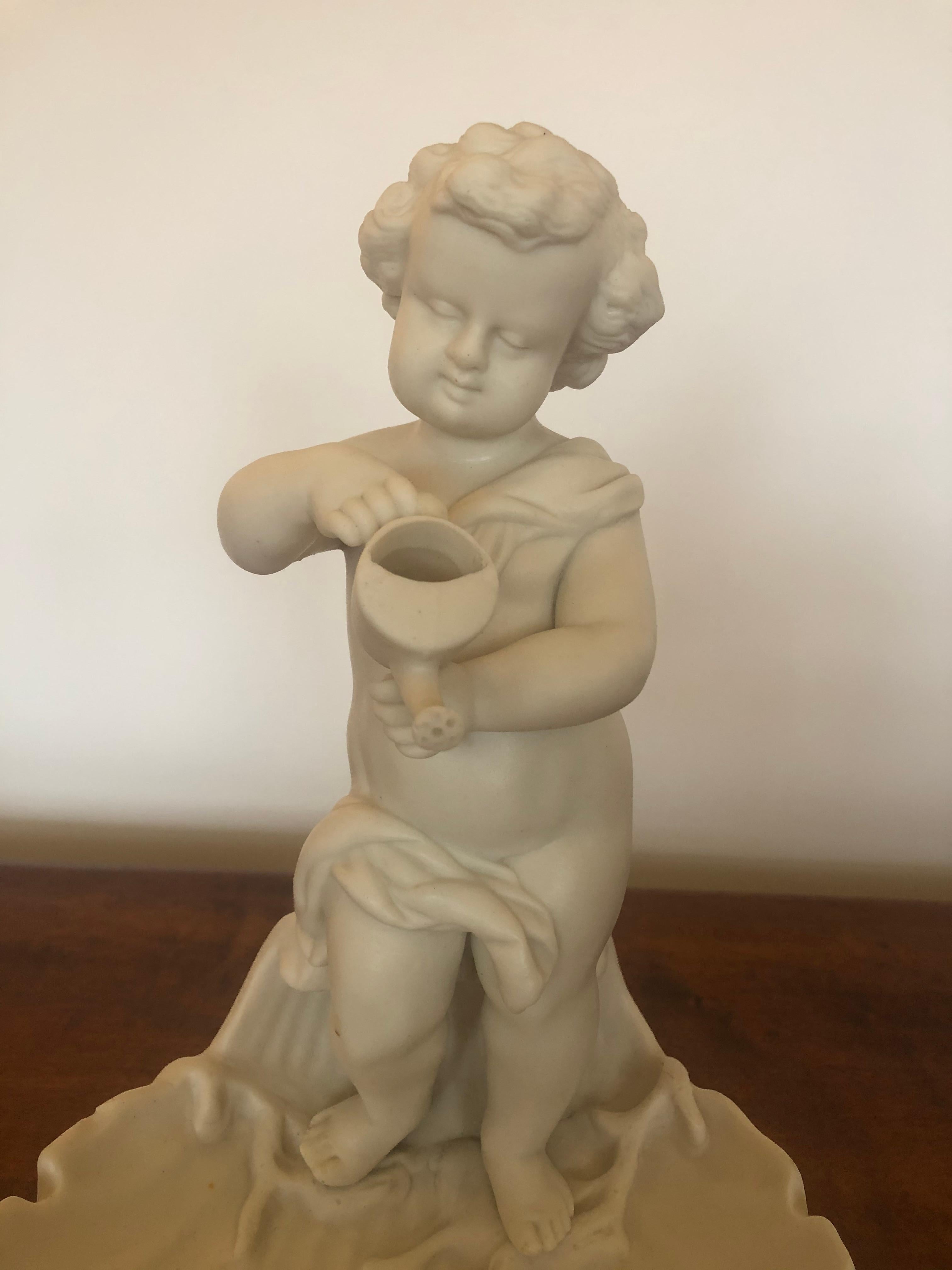 Magica scultura vintage in porcellana di un adorabile putti con annaffiatoio, appollaiato sul bordo di un piatto smerlato a forma di conchiglia.