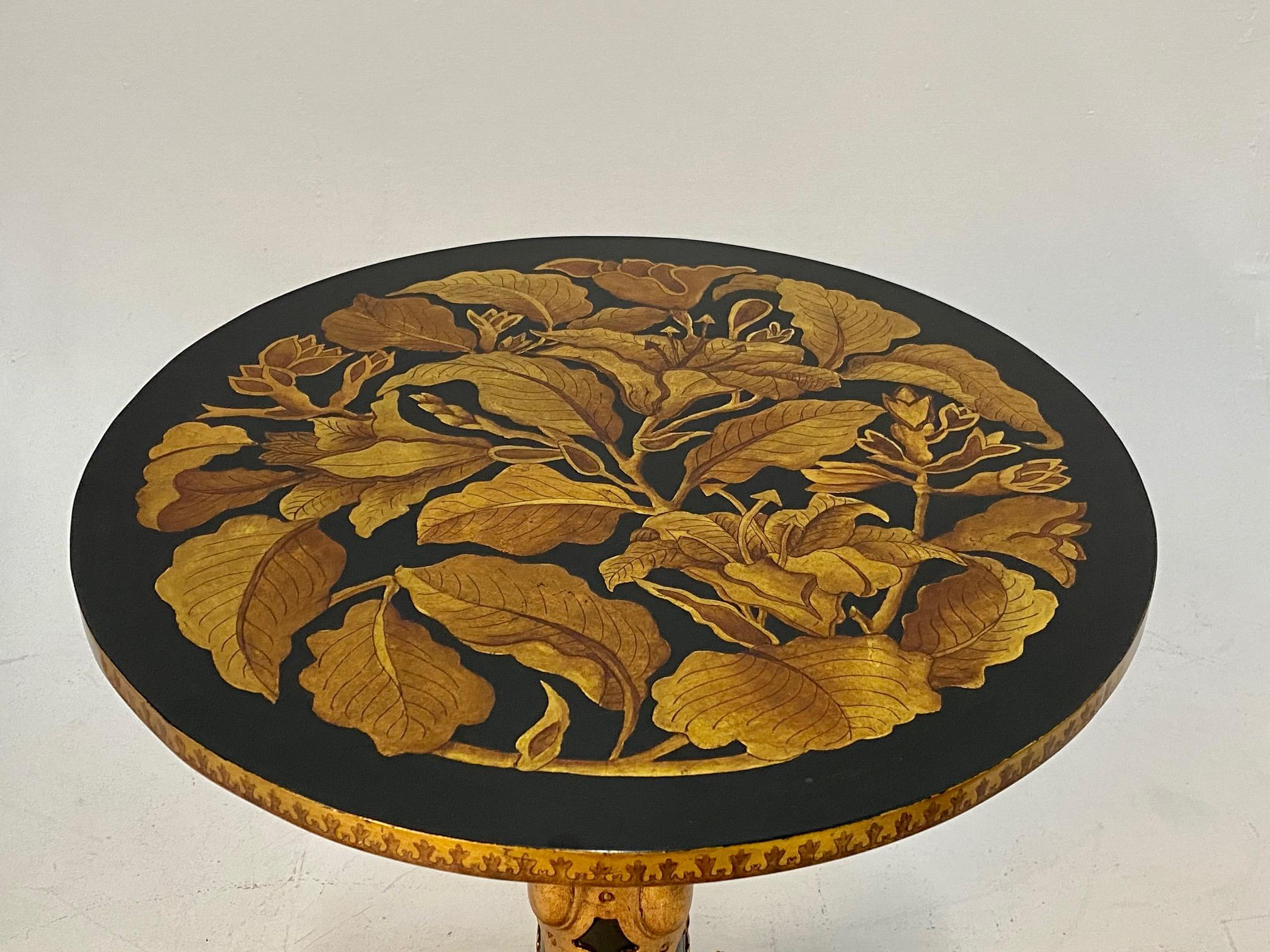 Sublimely decorated hand carved and painted round side or end table with striking black and gold color combination, having 4 curved feet, raised gilt decoration on column and feet, and gorgeous leaf motife embellishments. Original label underside.