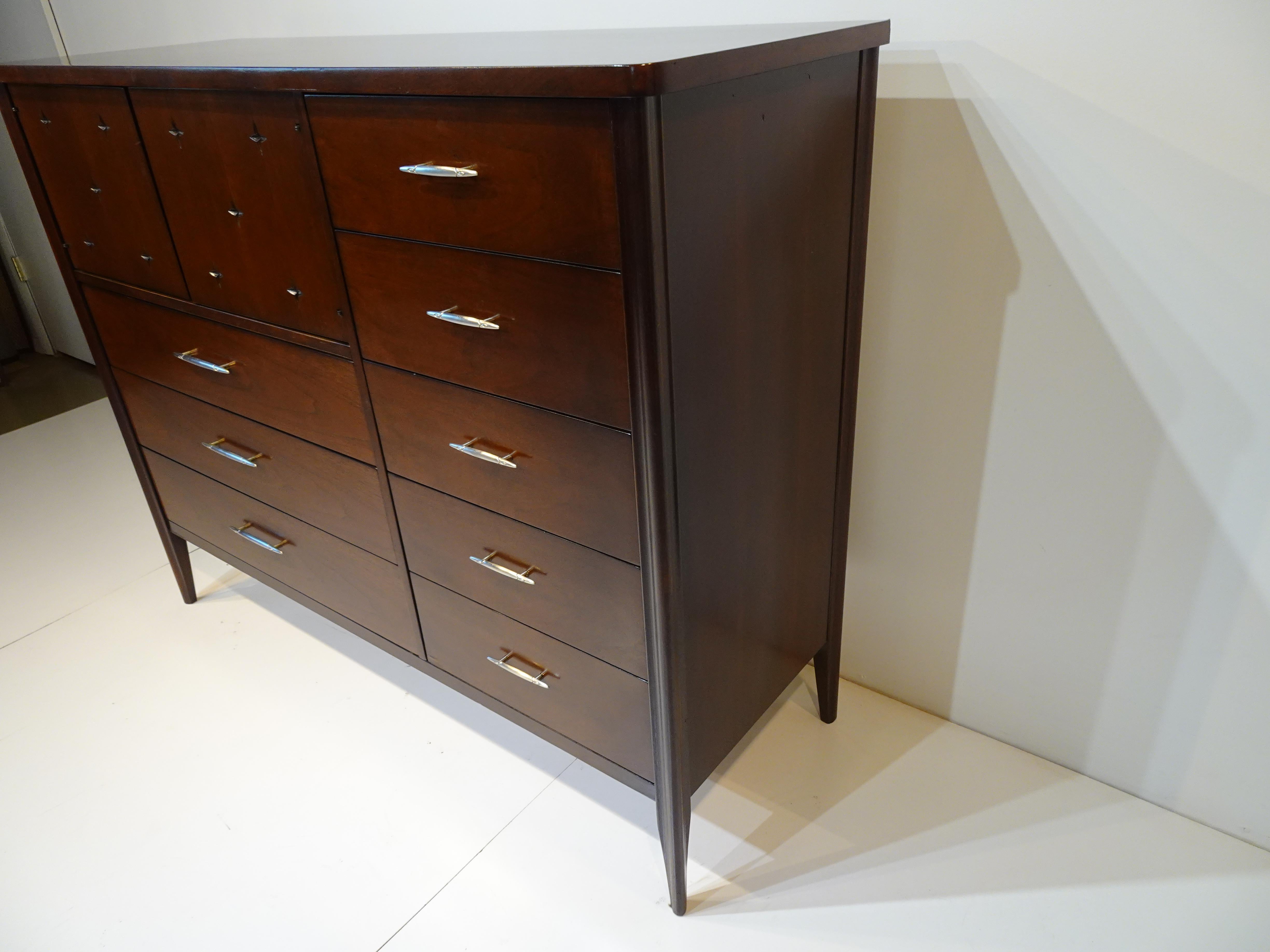 A dark walnut / ebony magna highboy chest with upper double doors with carved designs to the door fronts reveals three compartments for folded items. Three larger lower drawers and to the right side a bank of five smaller drawers all having polished