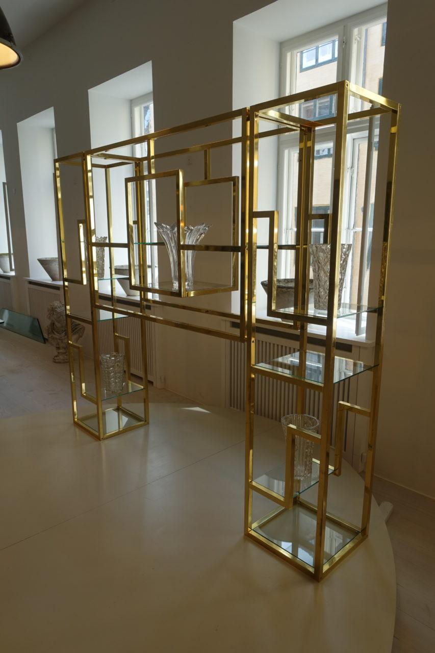 Large, handsome, distinctive, and sculptural vintage brass shelf unit, with numerous glass shelves, from 1960s France. This bookcase / display unit is divided into 3 sections compiling two high units, 1 on each side and a more elongated part in the