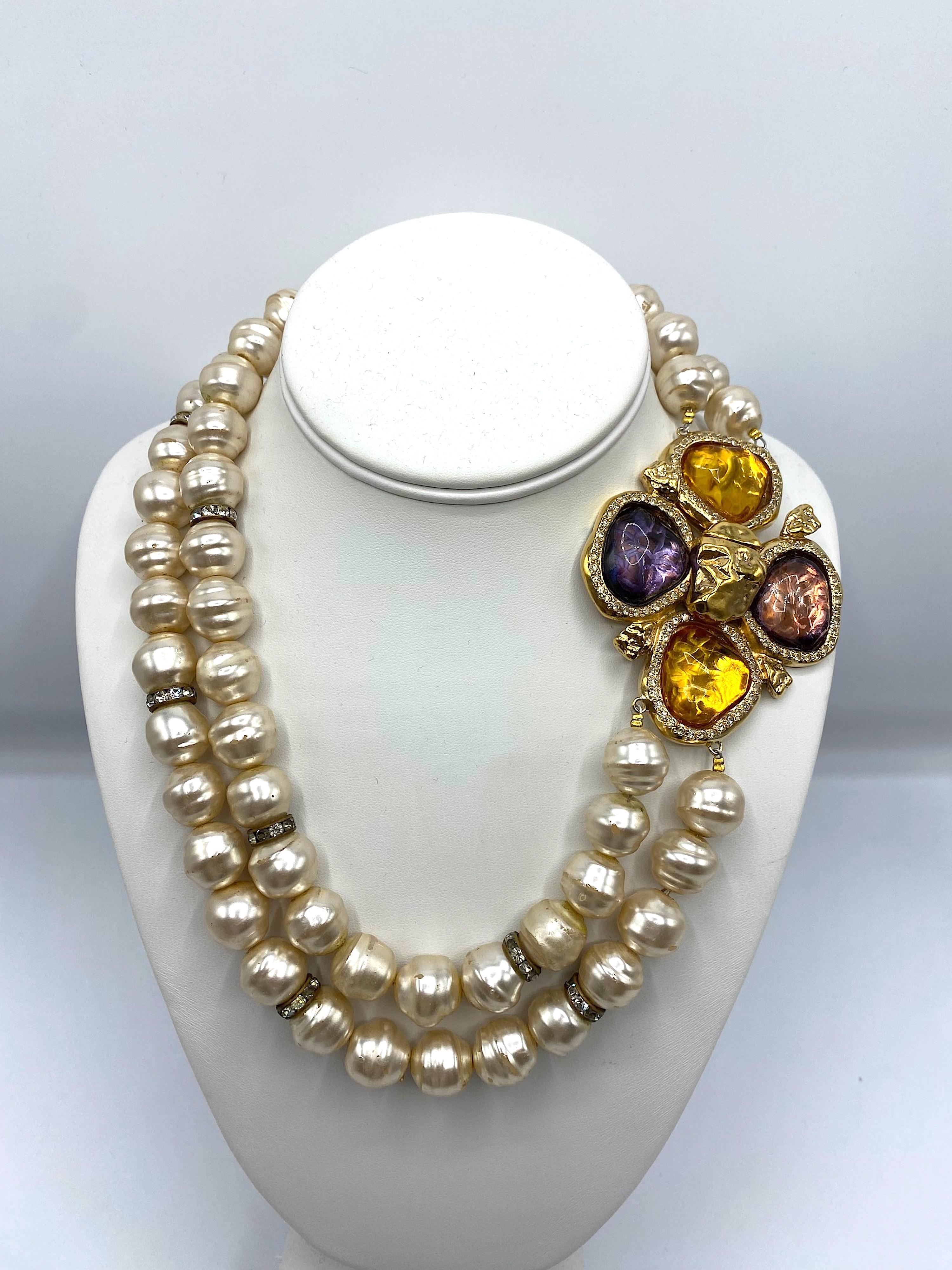 Questa collana di perle vintage degli anni '80 Robert Goosens for Yves Saint Laurent è un gioiello straordinario. Il design a due fili aggiunge dimensione ed eleganza al pezzo, mentre la chiusura a fiore in resina colata è un elemento di spicco. La