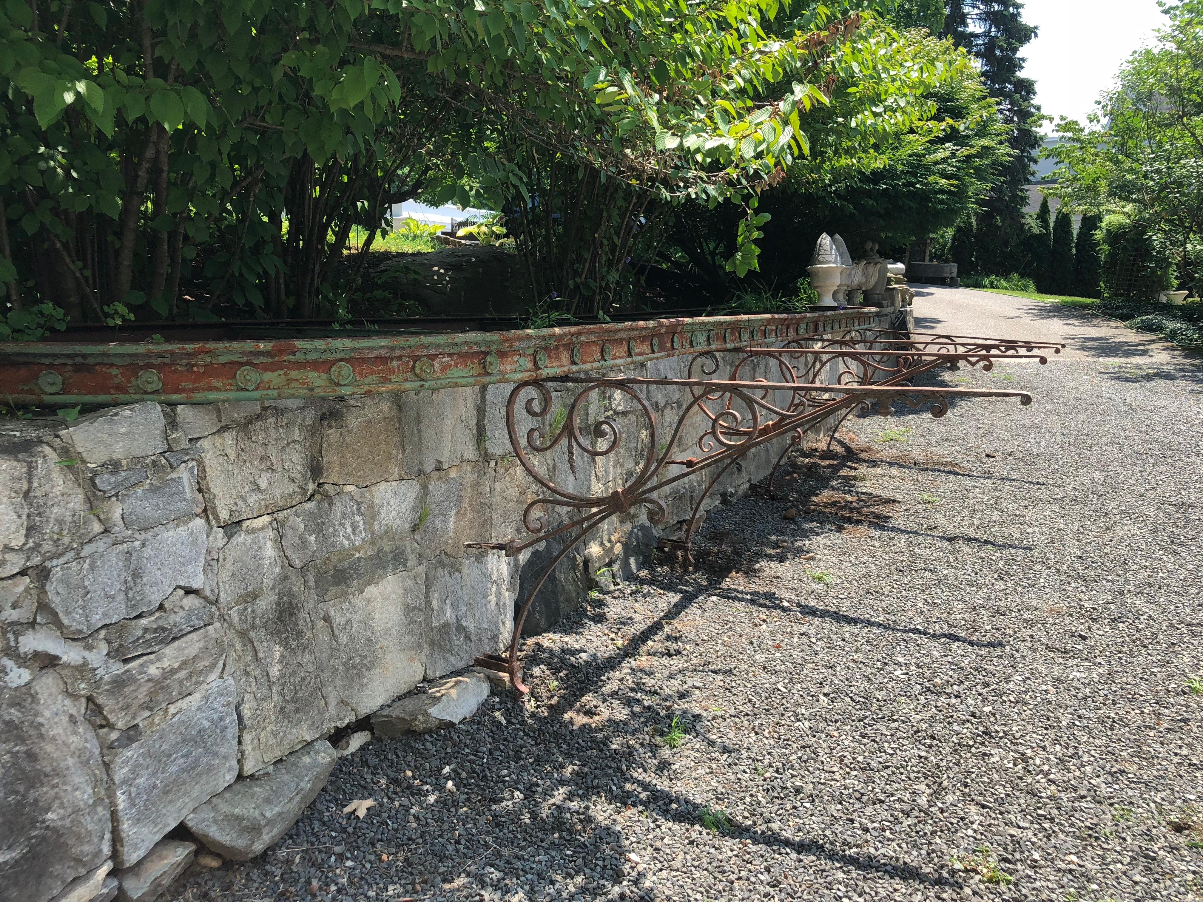 This is truly a very special piece! Sourced from a bistro in Lyon, France, this massive curved-end wrought iron pergola is 24 feet long and features decorative rosettes, its original paint with heavy surface rusting throughout, and four enormous