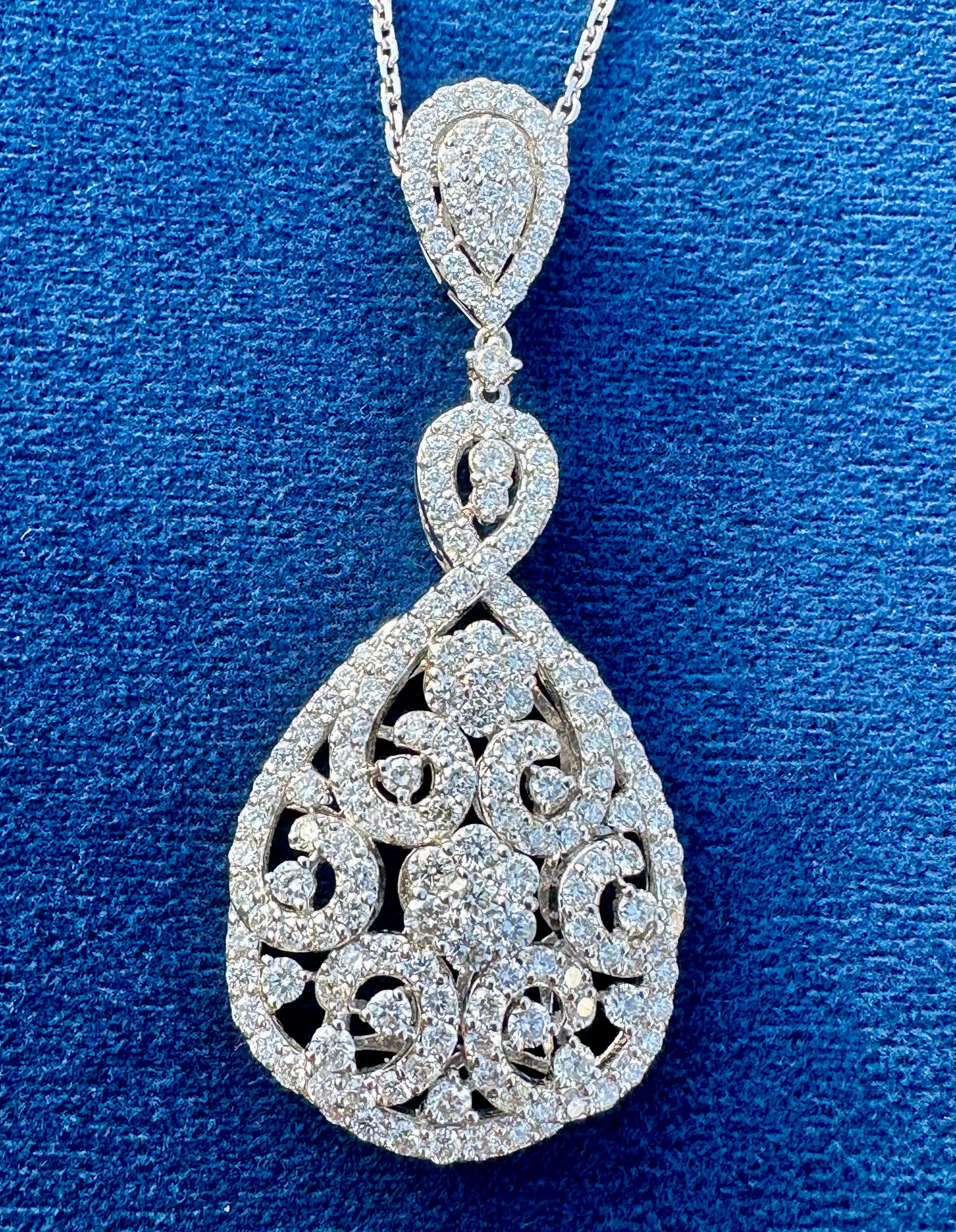Very elegant, ladies 18 karat white gold diamond cluster pendant features a slightly domed center with an array of round brilliant diamonds in a pear shape. Two diamond flower motif clusters are surrounded by fancy swirling motifs cascading