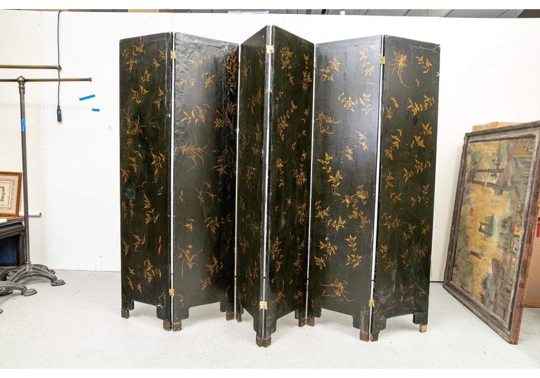 A six panel screen in black paint with overall gilt scrolled and carved and painted wood applied low relief decoration with some Mother-of-Pearl details. Scenes with pavilions and figures walking along paths in landscapes with tall trees, sages in