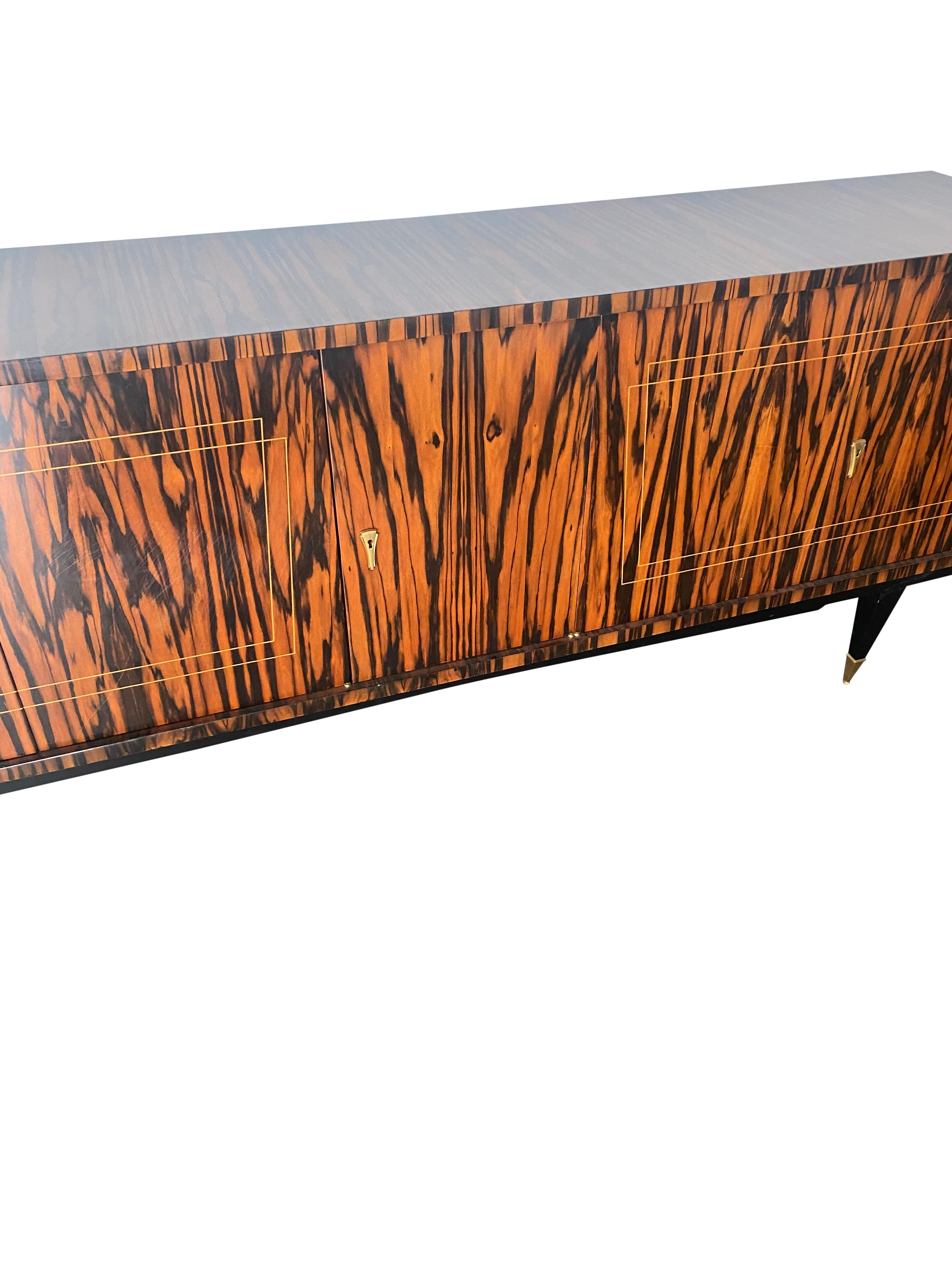 A truly unique master statement piece. European (likely French) credenza constructed of what appears to be rosewood or zebra wood with elegant brass detailing. Ample storage space consisting of interior shelving, housed behind three doors each