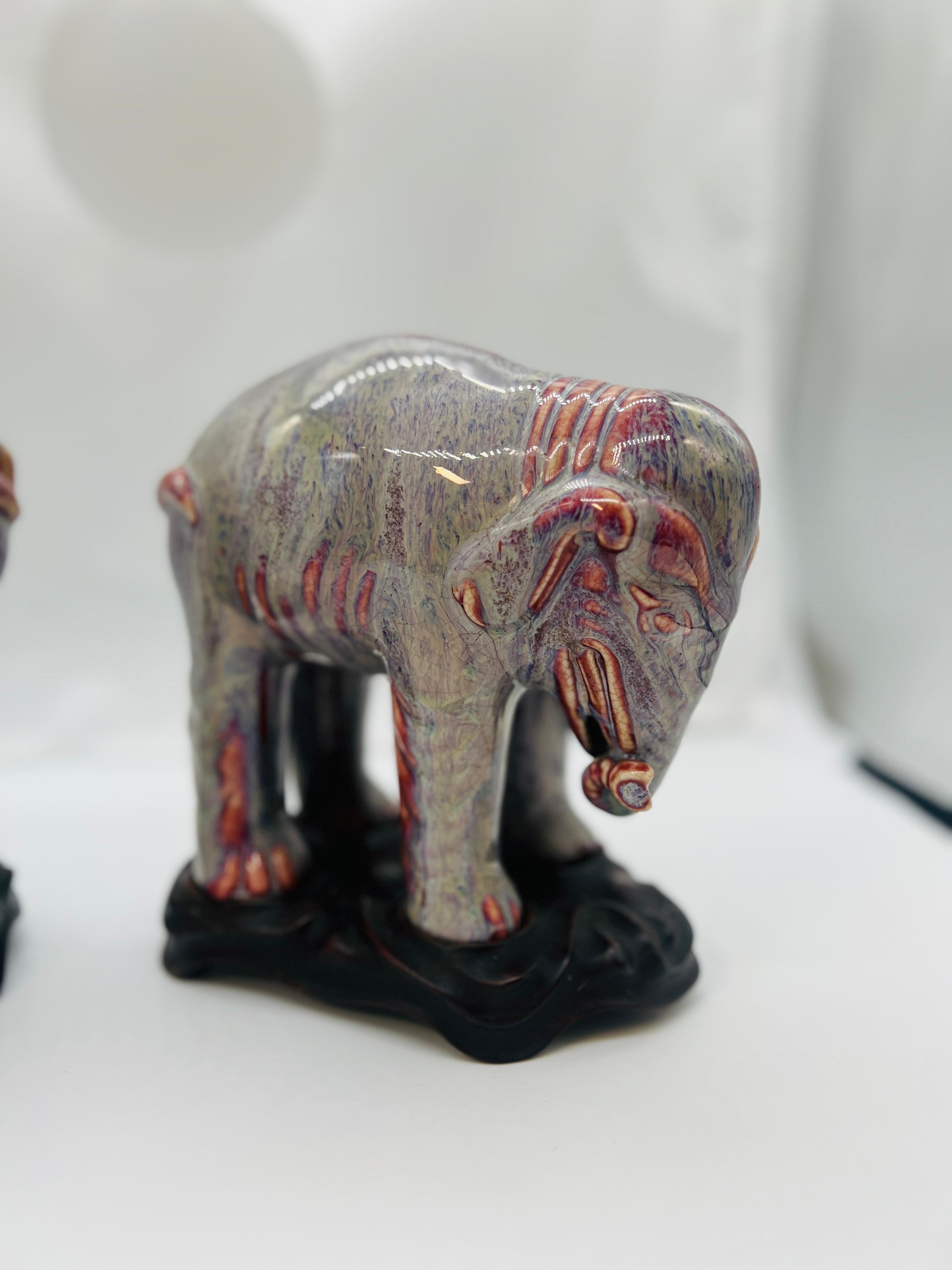 Chinese, 19th century or earlier.

A PAIR OF CHINESE PORCELAIN FLAMBE-GLAZED ELEPHANTS. 

Each elephant is a modeled mirror image - with an arched back and curling trunk. The entire piece having a craquelure flambe glaze in a VERY unique color
