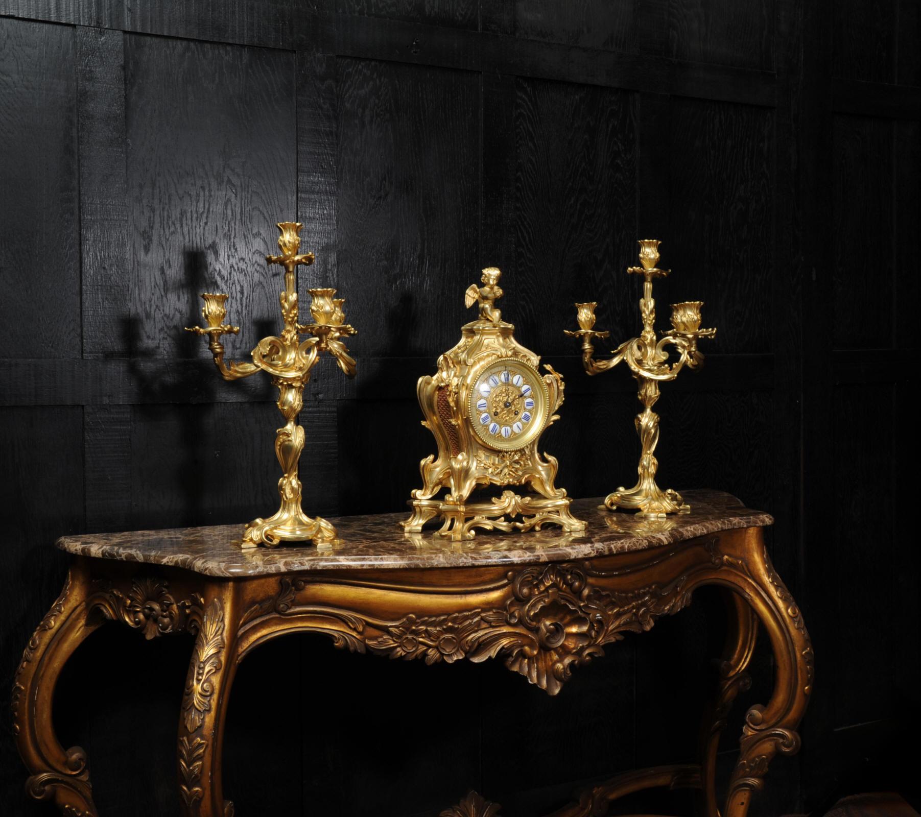 A very large and fine antique French clock set, circa 1880. It is of Rococo design in the manner of Juste Aurele Meissonier and boldly modelled in gilt bronze. Waisted keyhole shape with acanthus leaf shoulders, 'C' scroll feet standing on its