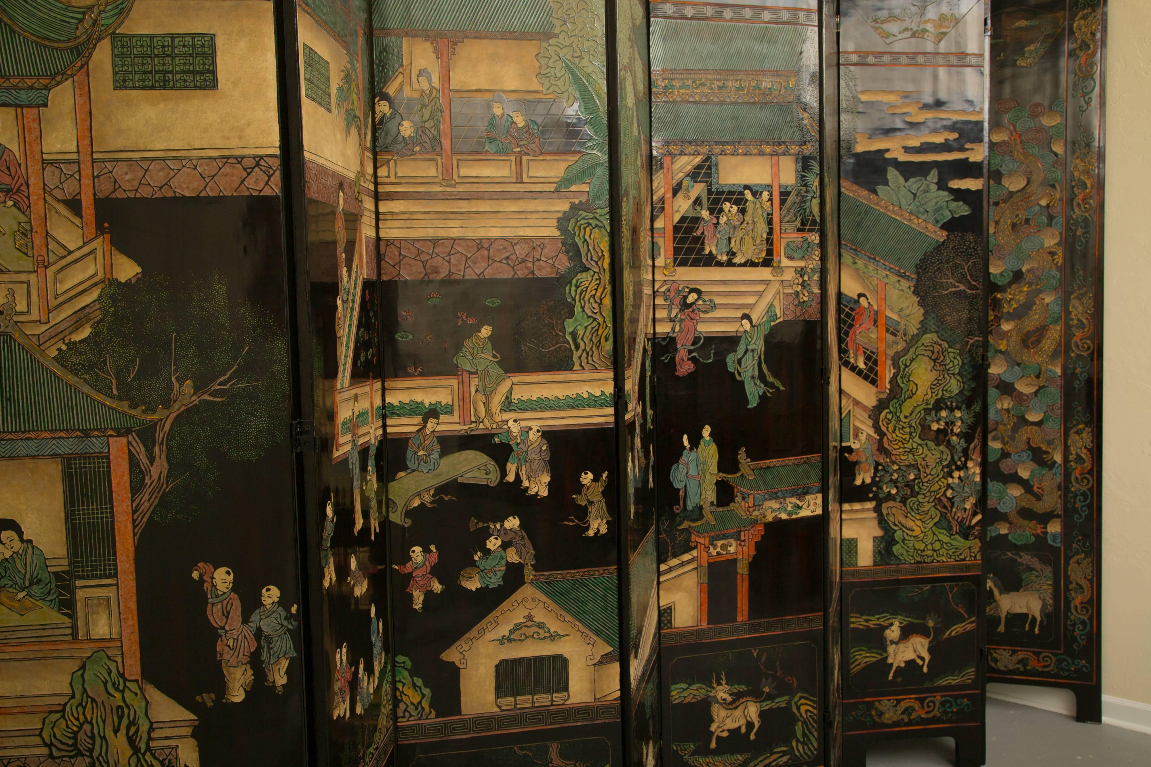 This stunning and sophisticated 12 black Coromandel screen is painted with detailed village scenes showing foliage, housing, walkways, and people -engaged in a variety of activities. The screen features a border with animals, foliage and other