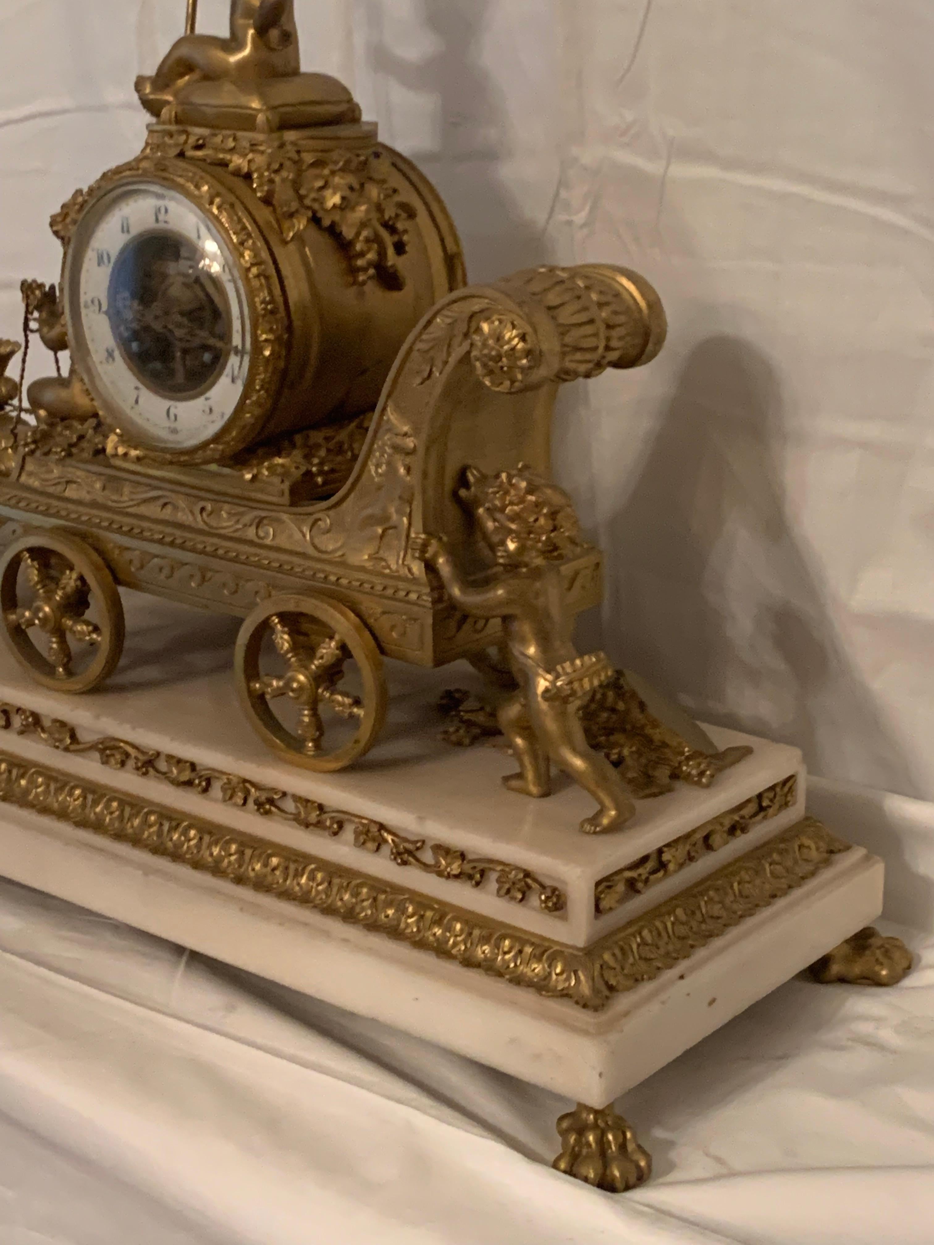 A fine antiques french gilt bronze and marble base clock representing cupids pulling  a chariot by rams.
the top of the clock is crowned by a cupid holding a ribboned sceptre at the back  a cupid push the chariot . Two rams are pulling the chariot