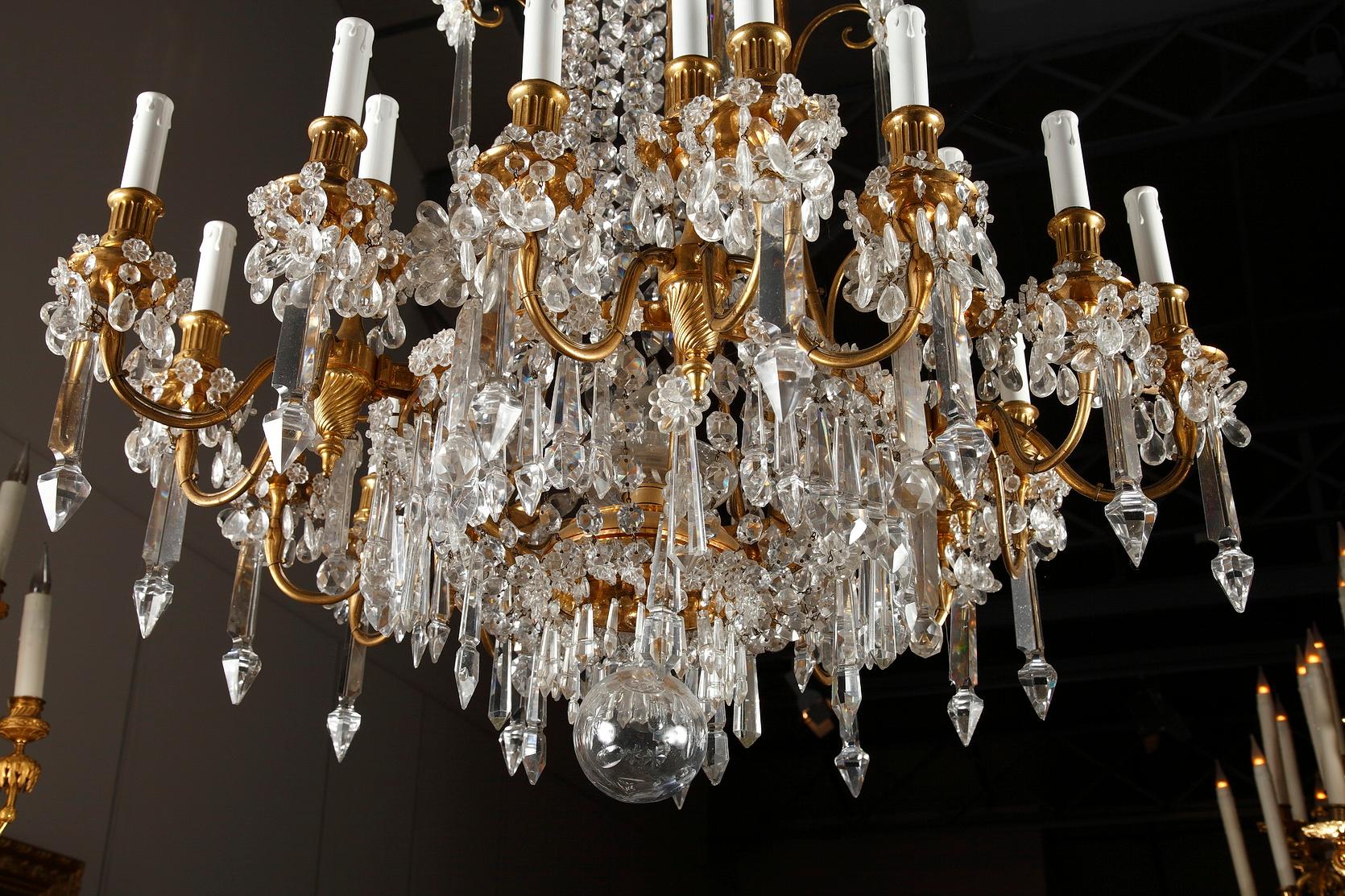 This magnificent chandelier, by the Crystal Manufacture of Baccarat, is made of gilded bronze and crystal and presents twenty lights. The tubular shaft composed by garlands made of crystal octogones is adorned with crystal flower crowns. The lower