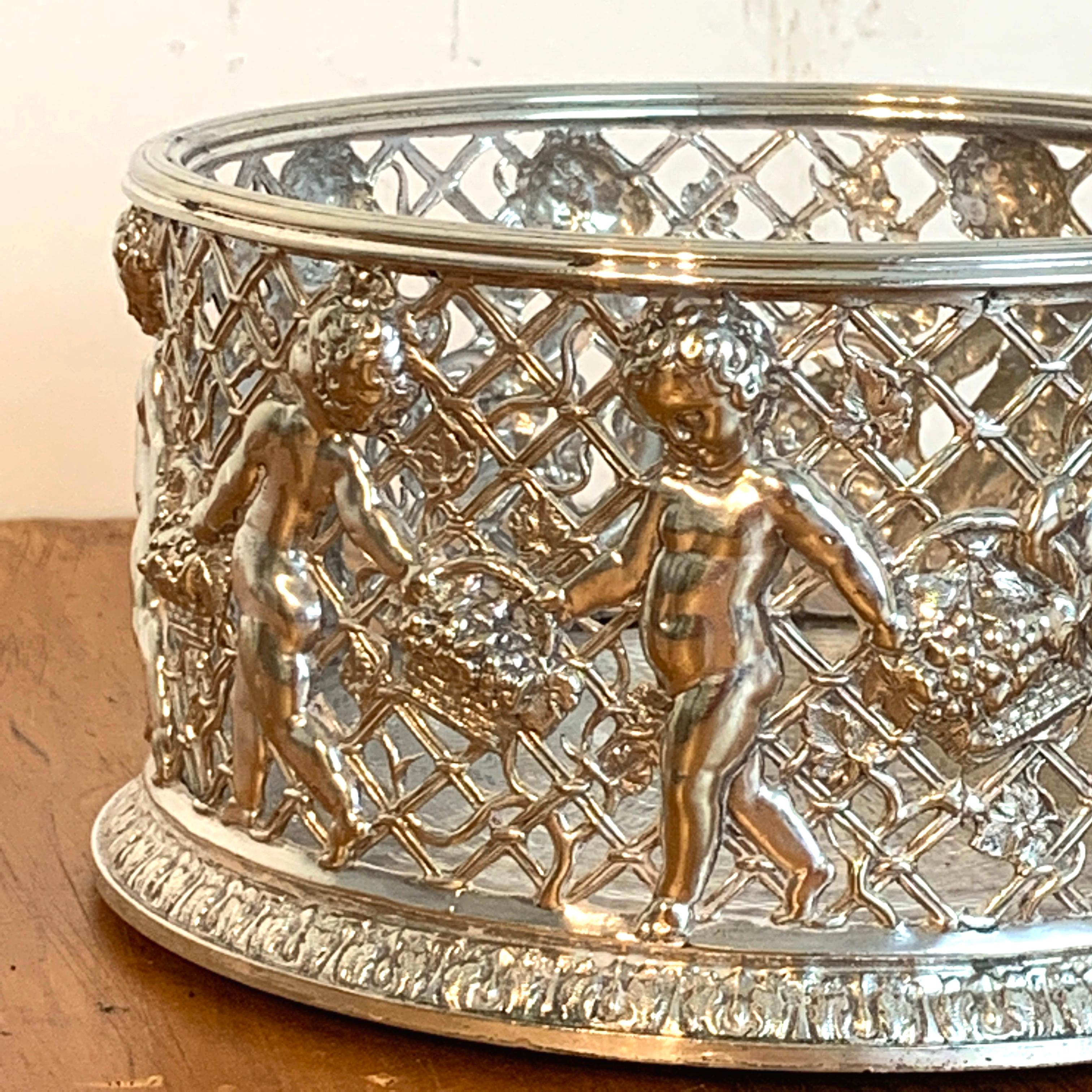 Magnificent English silver plated putti motif large wine coaster, attributed to Elkington. With pierced body with 9 frolicking draped babes with baskets of flowers, engine turned bottom with hardwood underneath. Apparently unmarked.