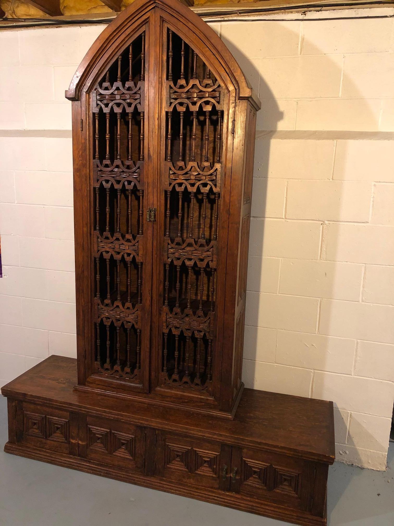 A one of a kind hand crafted ornately carved mahogany bookcase from New Orleans having tall church like arched Gothic style shelving unit with filligree doors with 5 interior shelves. The top is 89.5 inches from floor to tip of arch and 13 deep. The