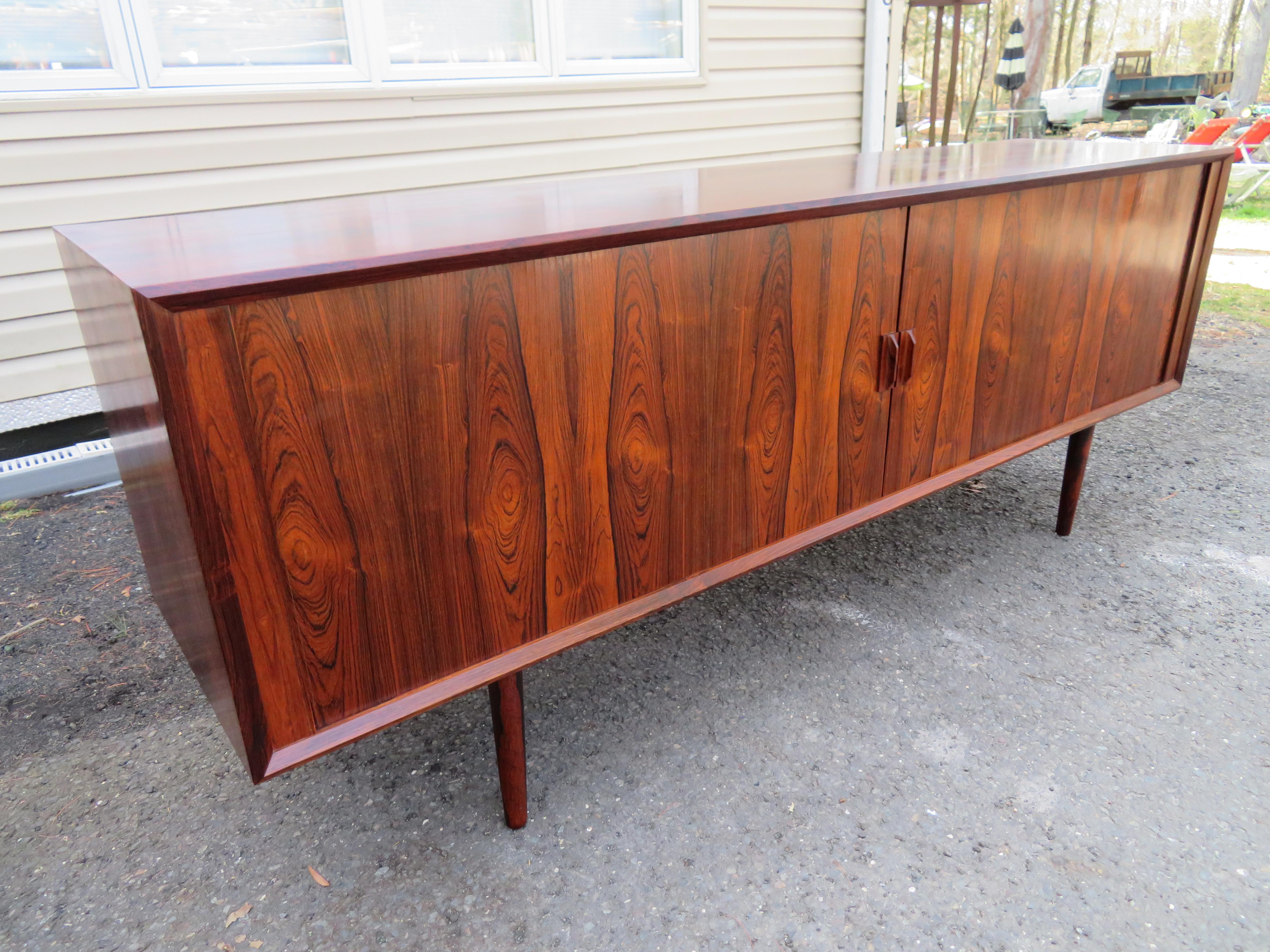 Wonderful Danish modern rosewood credenza by designed Ib Kofod-Larsen manufactured by Faarup Mobelfabrik. This piece features beautiful Brazilian Rosewood graining, tambour doors, adjustable shelves and four green felt-lined drawers. This one has