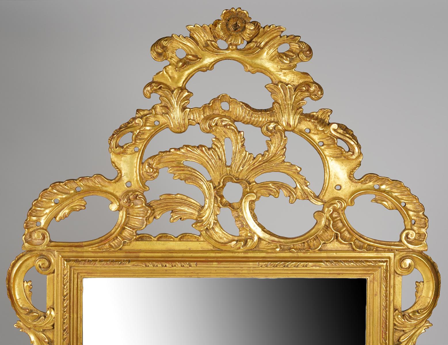 This elaborately carved giltwood mirror by Palladio dates to the mid-20th century and is fashioned in the rococo style with impressing foliate scrolls centering a rose at the very top. The quality of the gilt is superior with a comnination of high