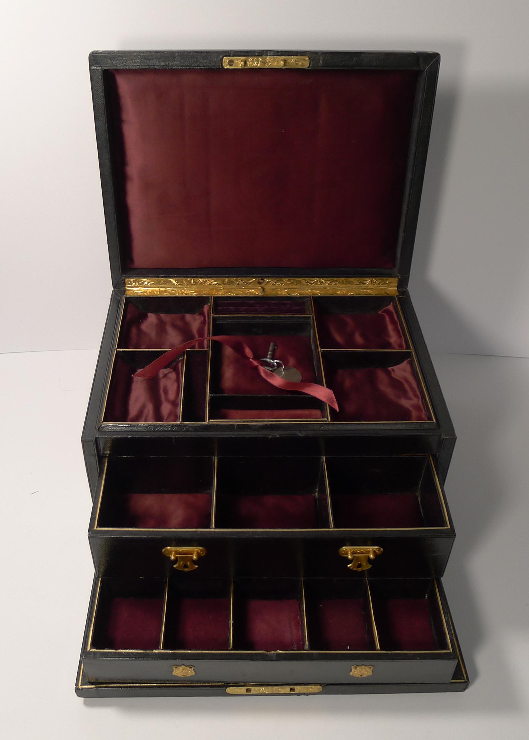 A top-notch large Victorian jewelry box covered in black leather with gold embossing and a fabulous inset gilded brass handle retaining the original gold finish, the front has a complimentary escutcheon.

The lid lifts to reveal a wonderful fitted
