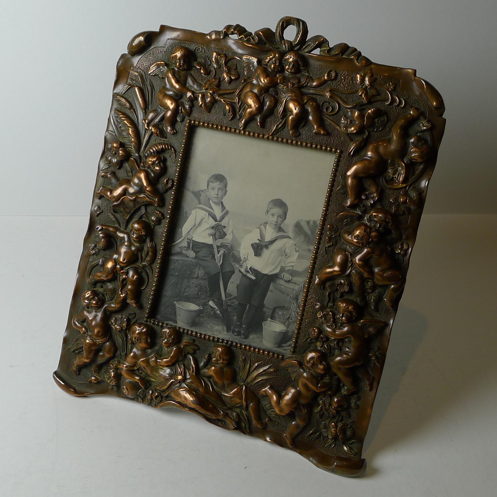 An outstanding antique French photograph frame made from cast mixed metals with the most amazing collection of cherubs gracing the front amongst a plethora of flora and foliate decoration, all finished with a combination of copper plate, brass and