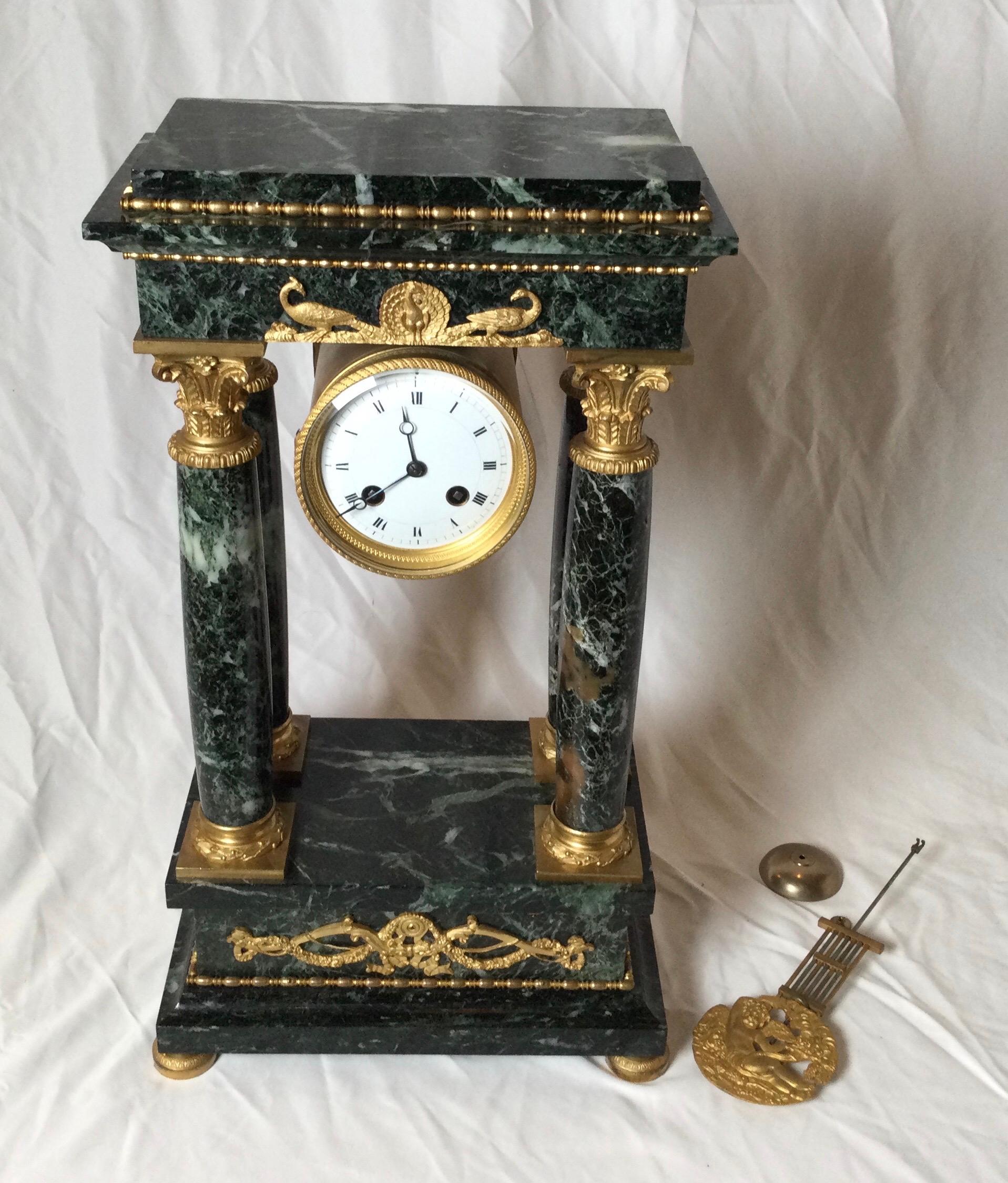 Elegant French Empire Portico clock with ormolu mounts. The classic four column form in a dark varigated green marble with detailed gilt bronze mounts and pendulum. The clock has been serviced and runs but might need adjustment after shipping.