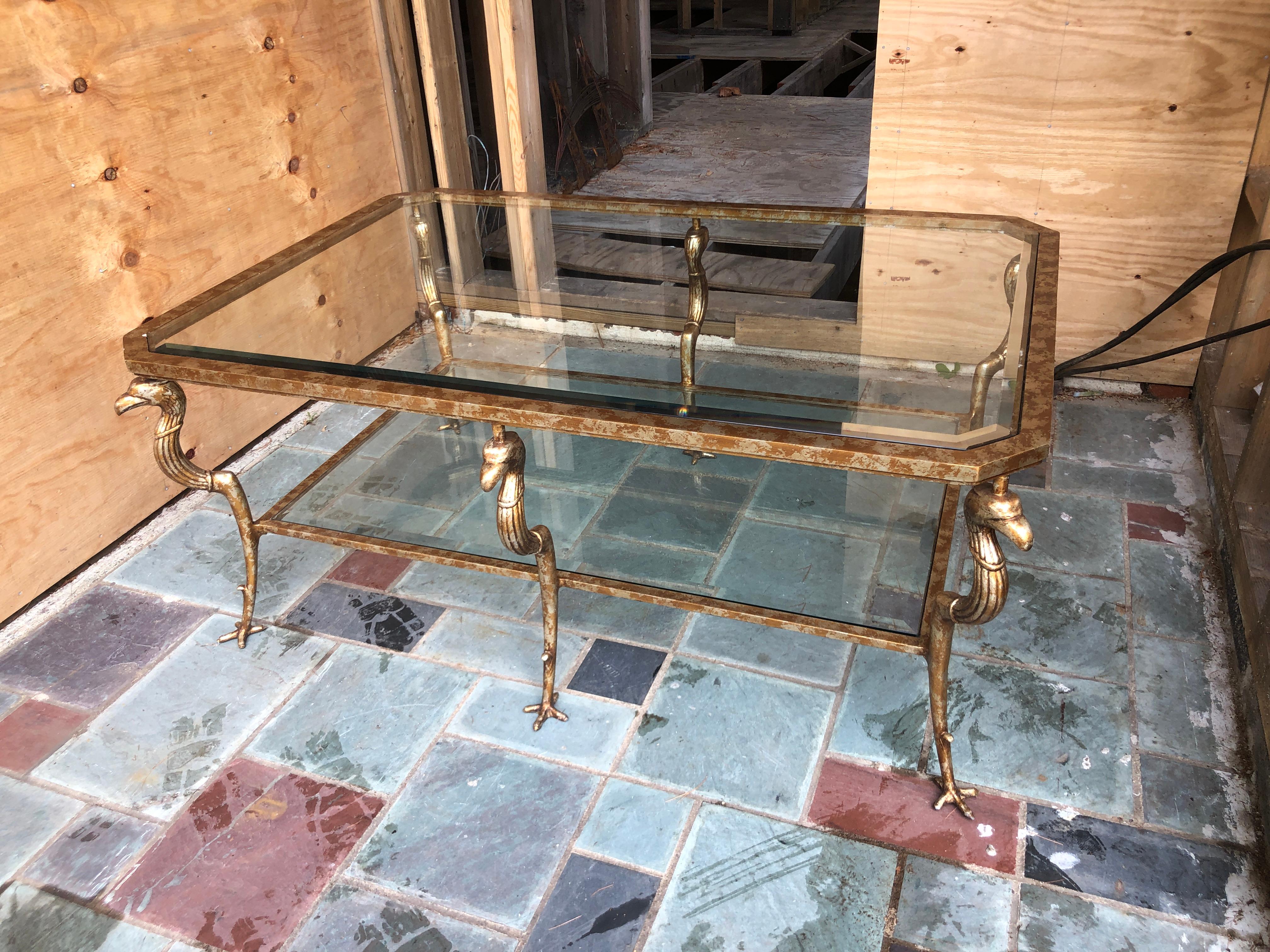 Marge Carson (American, founded 1947), contemporary. Rectangular-form cocktail or coffee table in the empire or regency taste, having a two-tier steel frame with antique gold finish, inset beveled glass, and rising on griffon-form supports with claw