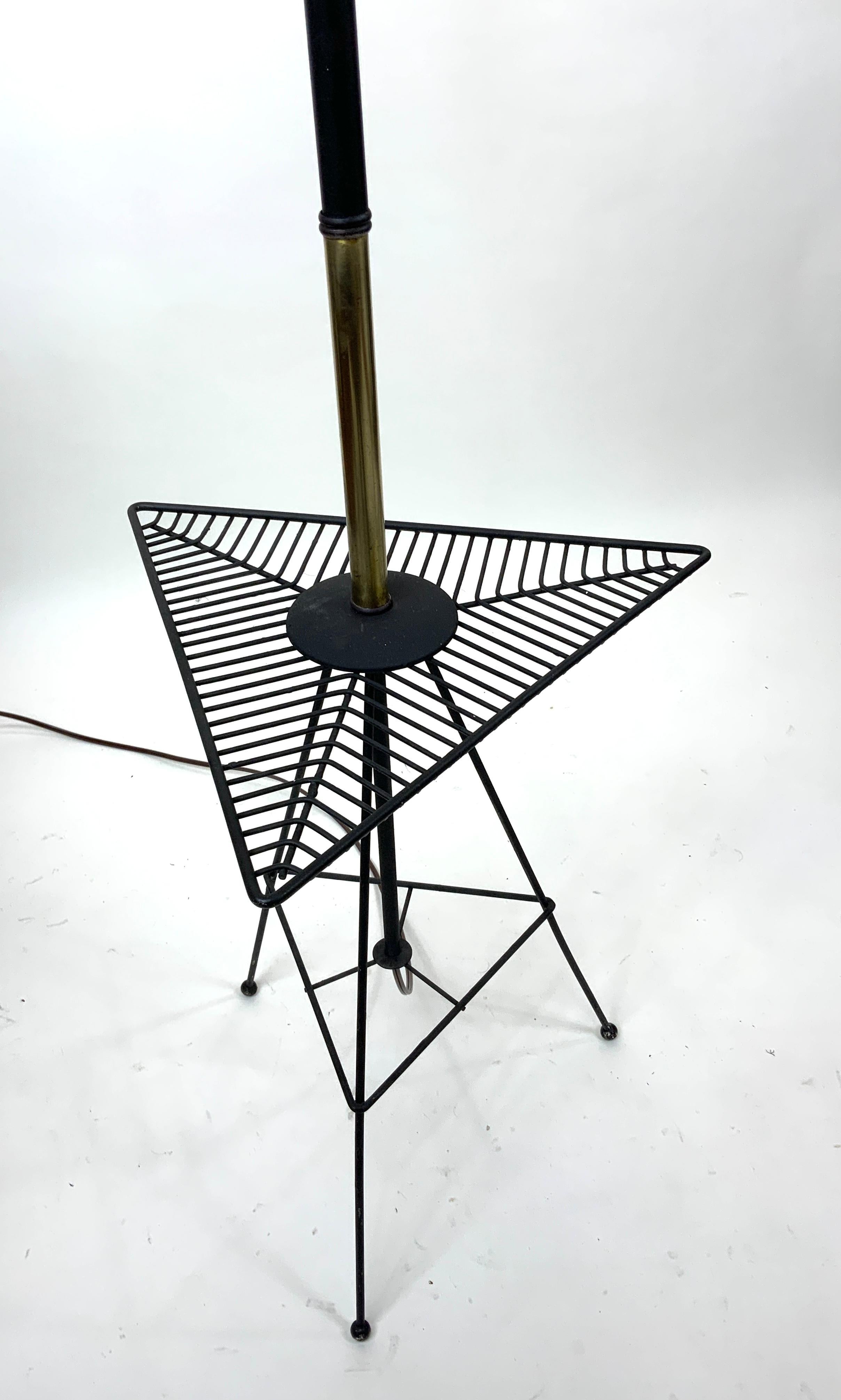 Lámpara de pie moderna de mediados de siglo con mesa auxiliar combinadas en una sola unidad. Estructura de metal patinado negro y latón.  Pantalla original de fibra de vidrio. Todo en muy buen estado.  ¡Gran look retro!

Altura:  62.25 in. (158.1