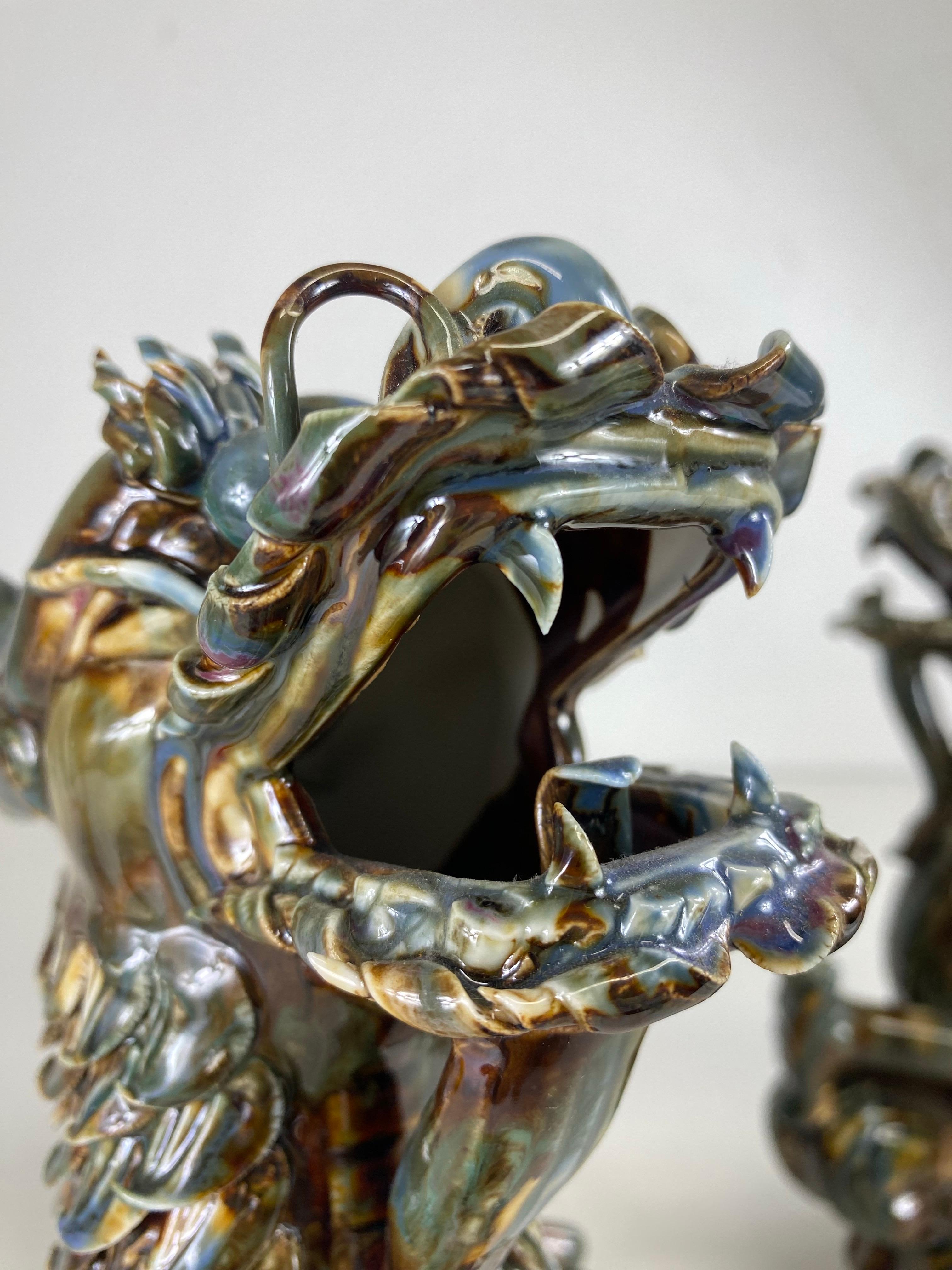 This is a mid-century vintage magnificent pair of large majolica pottery dragons. This pair of Chinese export dragons have a magnificent majolica glaze to the surface with deep tones of olive green, brown and Amber. The dragons are expertly crafted