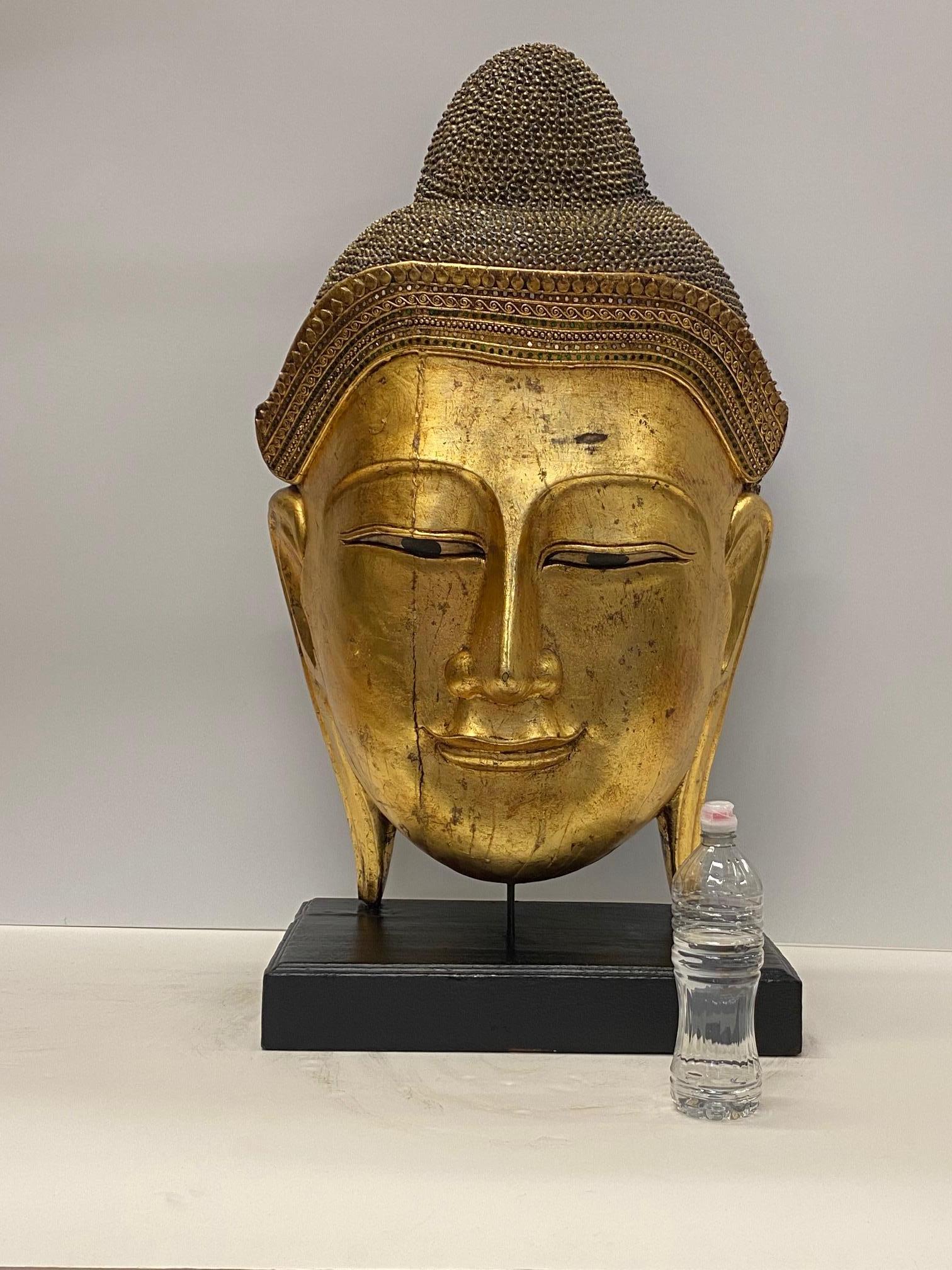 Impressively large gilded carved hardwood Thai Buddha head having gold leaf and meticulously detailed decoration with inset jewels. Beautiful serene expression and simple black base.