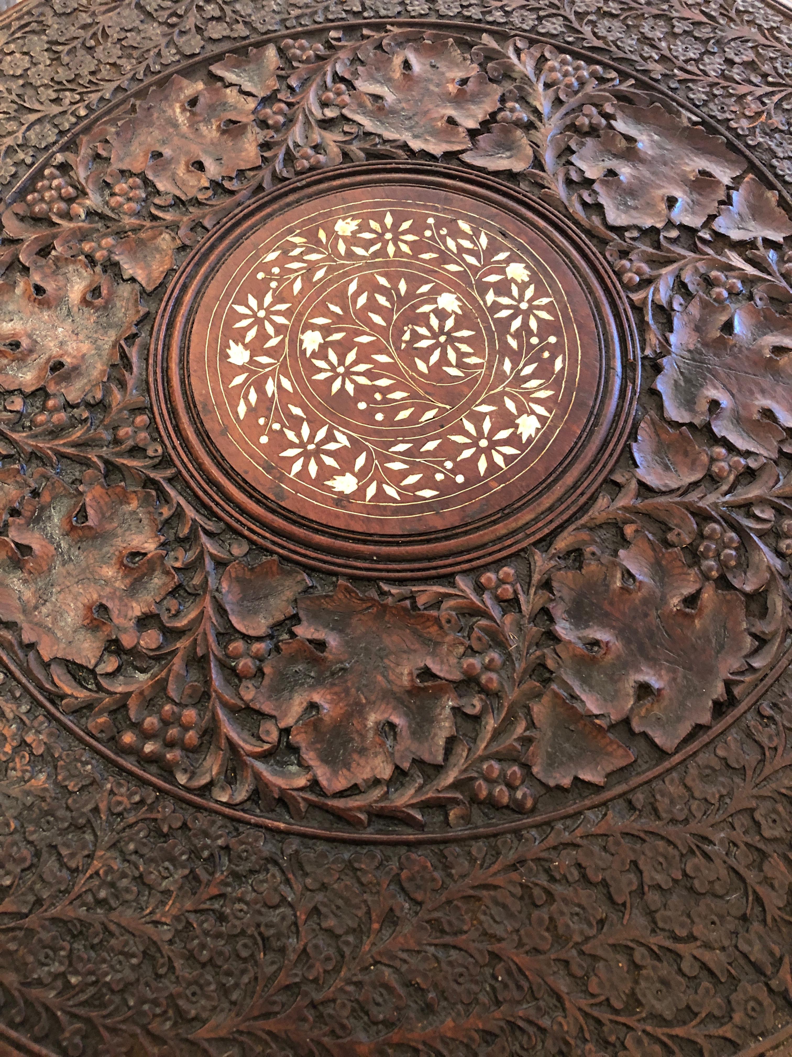 Intricately carved Anglo Indian round side table having round top with beautiful central shell inlay and an octagonal base. Base accordians flat for moving or shipping and top comes off.