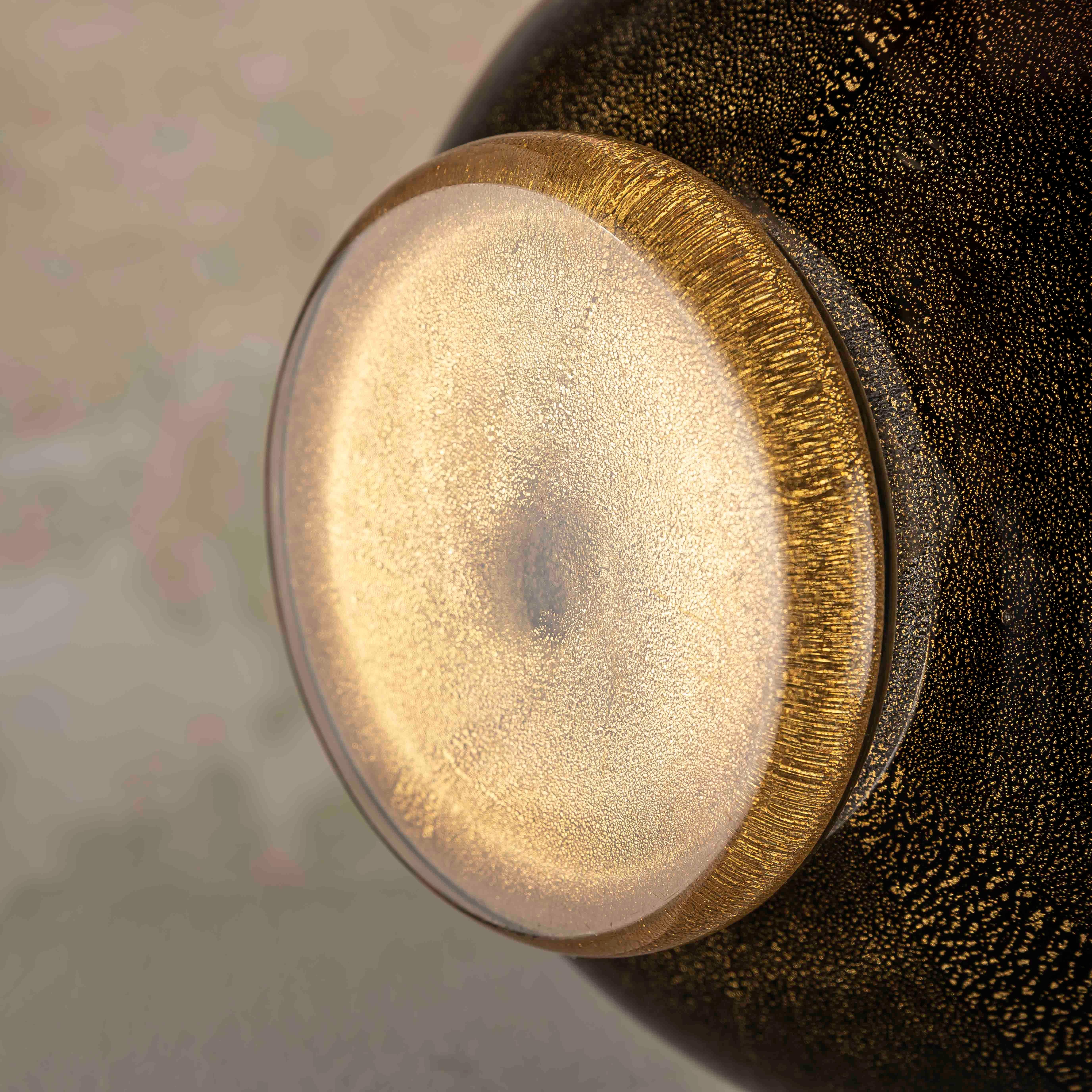 Questo vaso in vetro nero con scaglie d'oro è un capolavoro che fonde senza sforzo l'opulenza lussuosa con la modernità sofisticata, evocando l'essenza di un design senza tempo. Ispirato allo spirito innovativo di Napoleone Martinuzzi, questo vaso