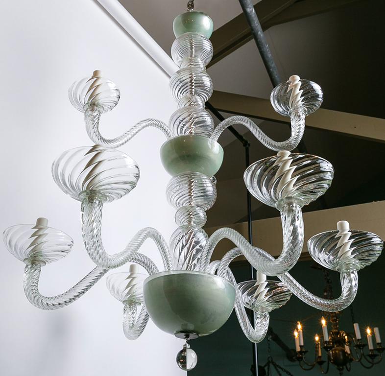 This beautiful Murano chandelier is both simple and showy at the same time. It is clear glass with a bit of a celadon color on its two bowls. It has a hand-blown twist motif throughout its arms and bobeches. A uniquely classic Murano light with a